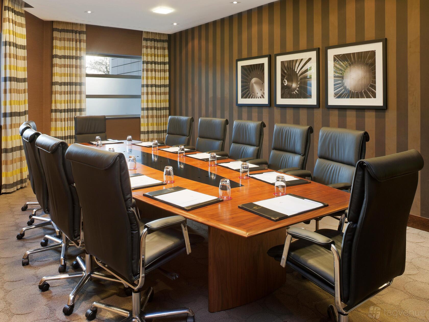 A boardroom with a long wooden table, leather chairs, notepads, and striped walls at Crowne Plaza London Gatwick.