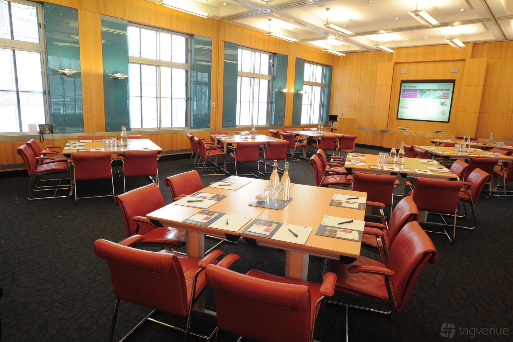 A meeting room with large windows, wood panel walls, conference tables, and red chairs at Broadway House Council Chamber.