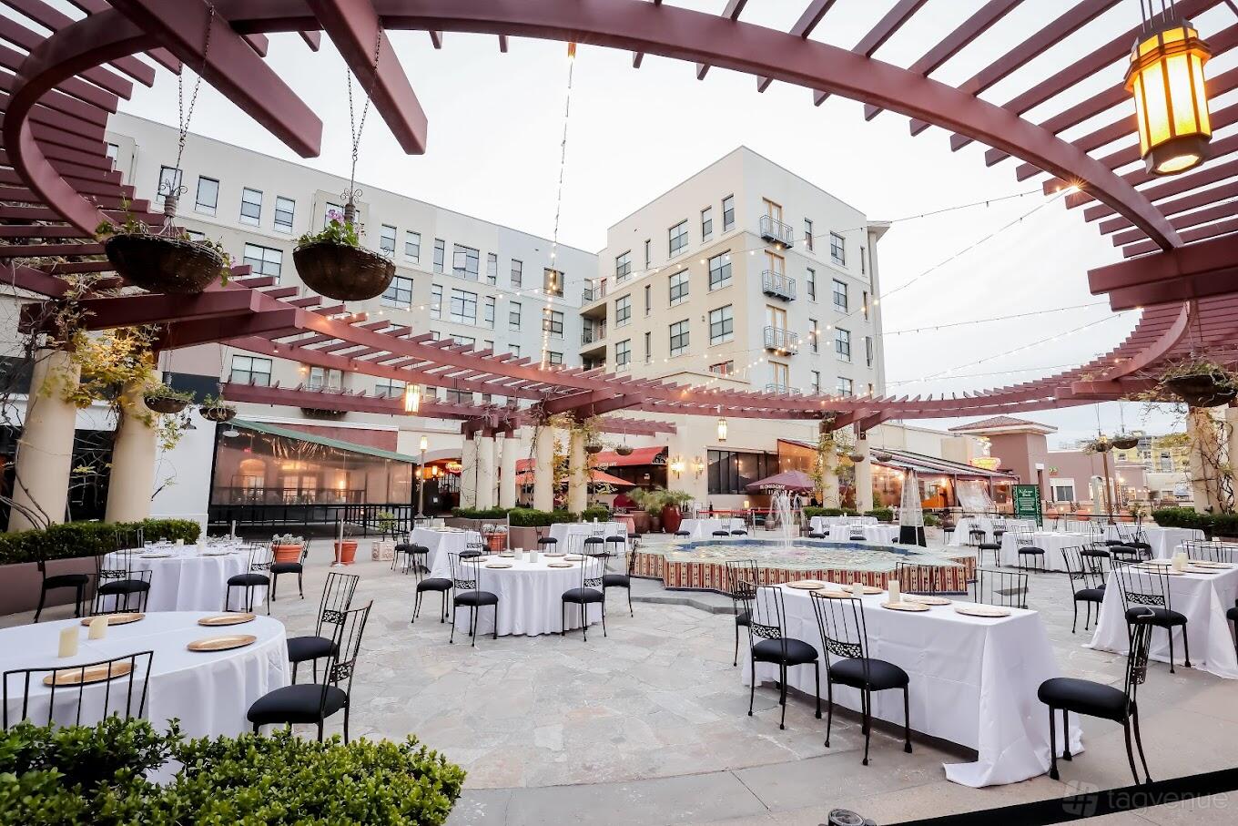 An outdoor terrace with hanging planters, string lights, and round tables with white linens at Noor Events.