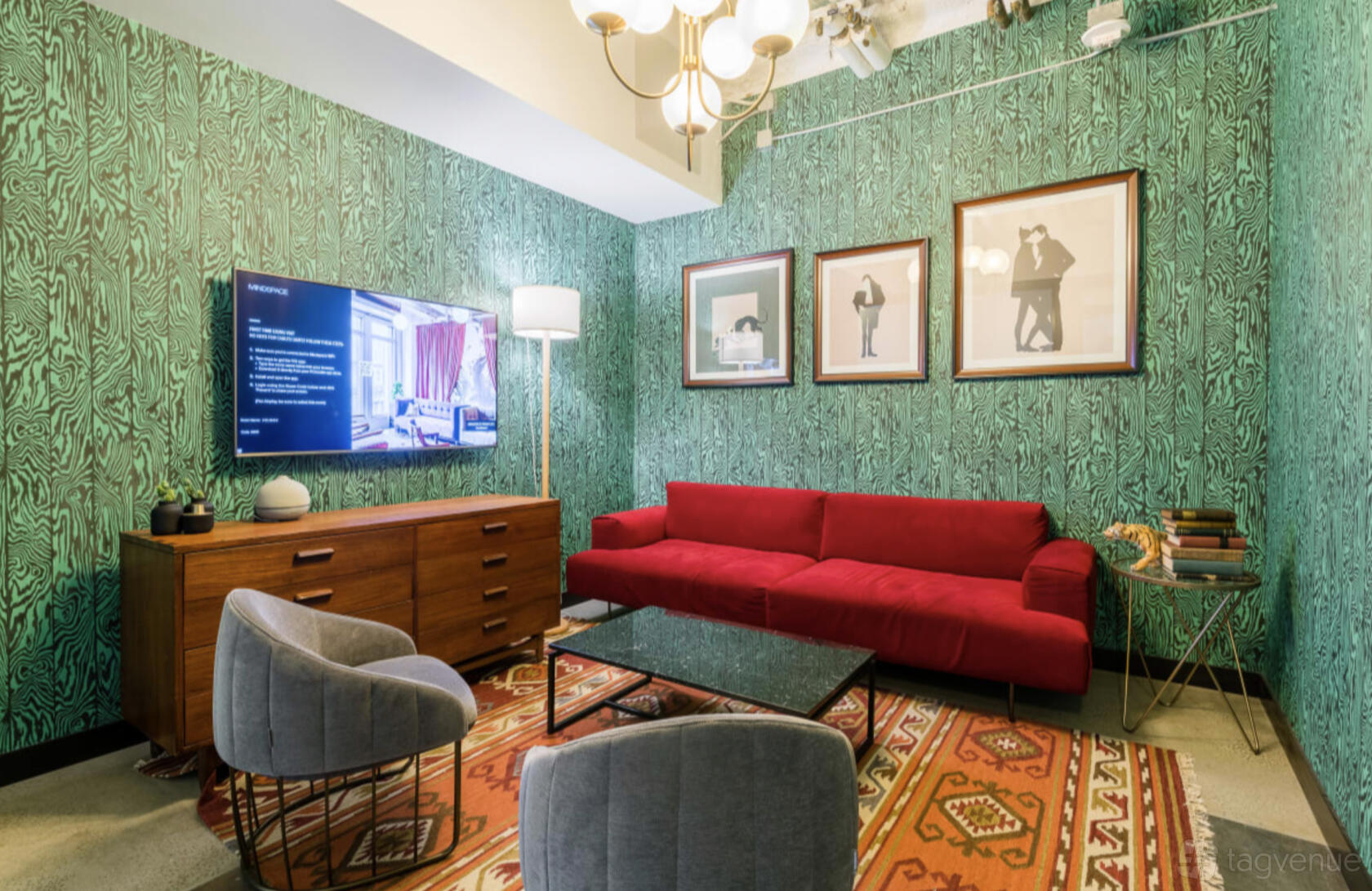 A coworking space lounge with a red sofa, patterned rug, green wallpaper, and framed artwork at Mindspace San Francisco.