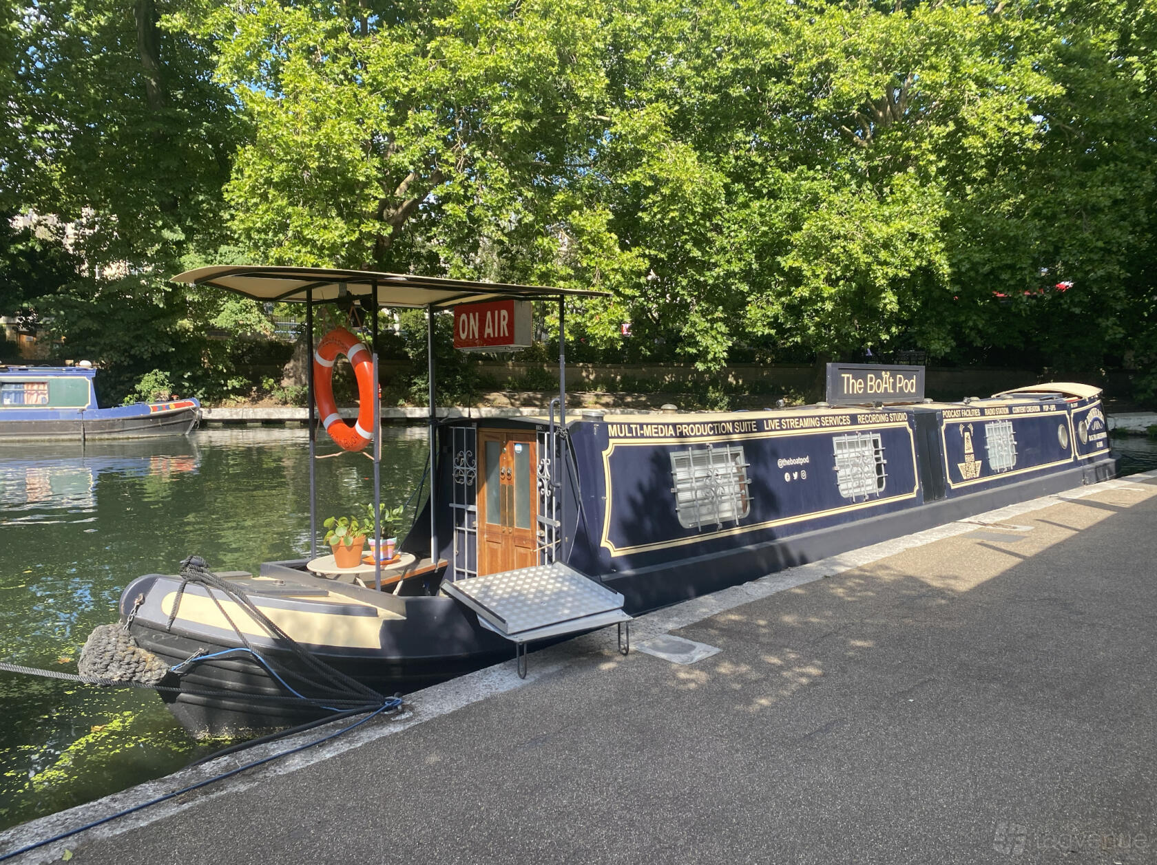 A canal boat recording studio with outdoor seating, potted plants, and an 'On Air' sign at The BoAt Pod.
