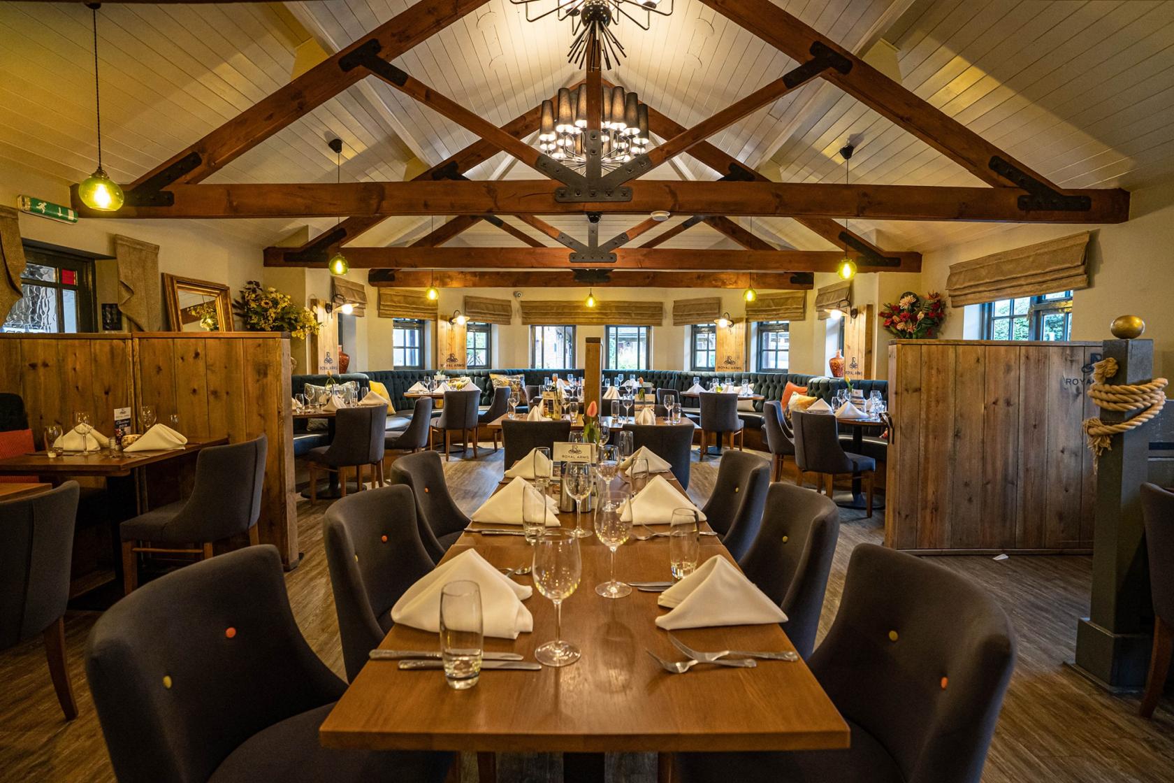 A hotel dining room with exposed wooden beams, chandeliers, and tables set with white napkins at Royal Arms Hotel.