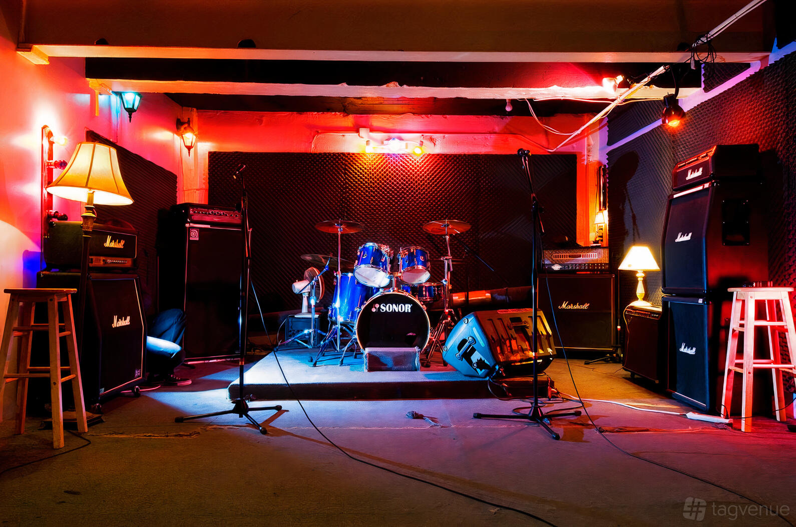 A recording studio with a drum kit, amplifiers, colorful lighting, and soundproofed walls at The Best Deal in Town.