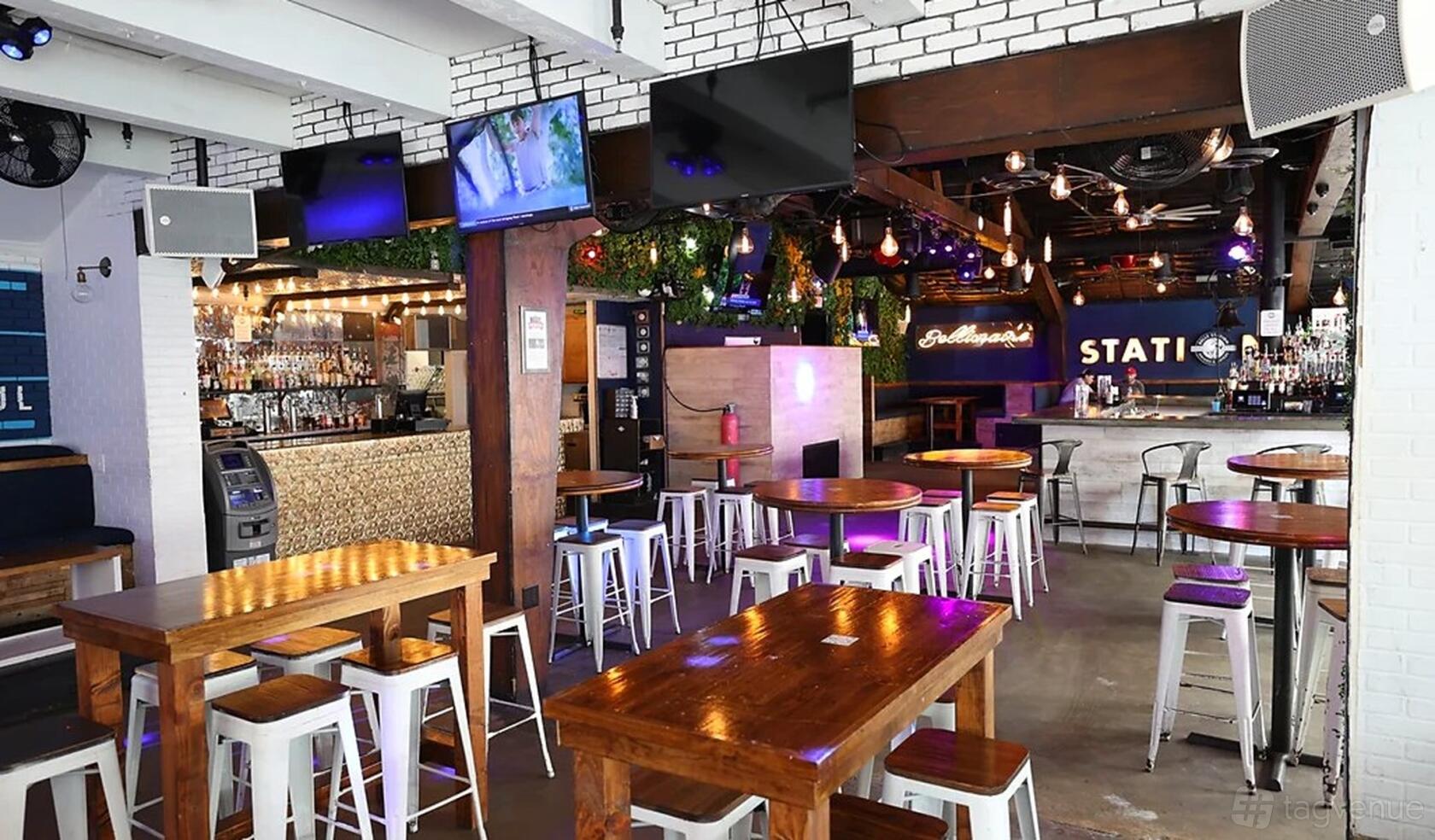 An event space in a restaurant with wooden tables, metal stools, exposed brick walls, and hanging string lights at Belle Station.
