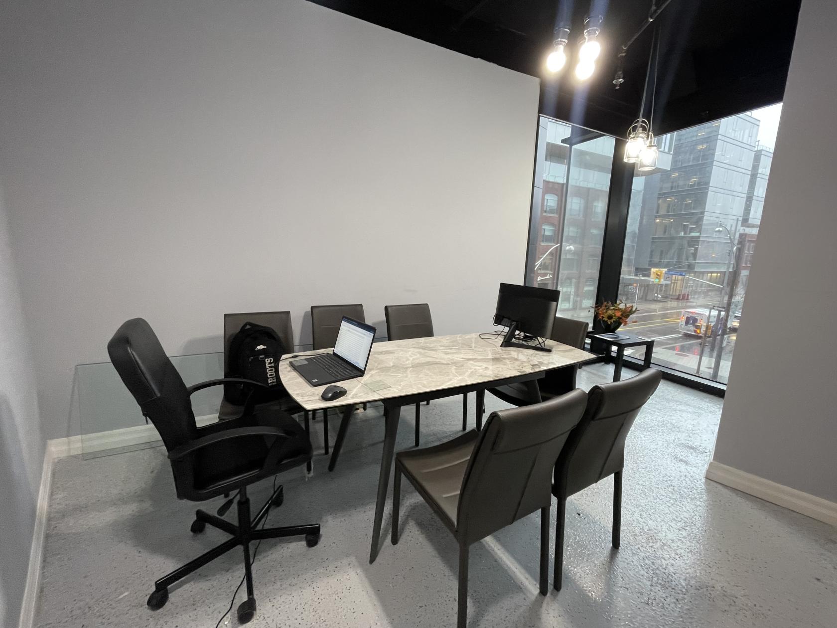 A meeting room with a marble conference table, office chairs, large window, and street views at Entrepreneurs Point.