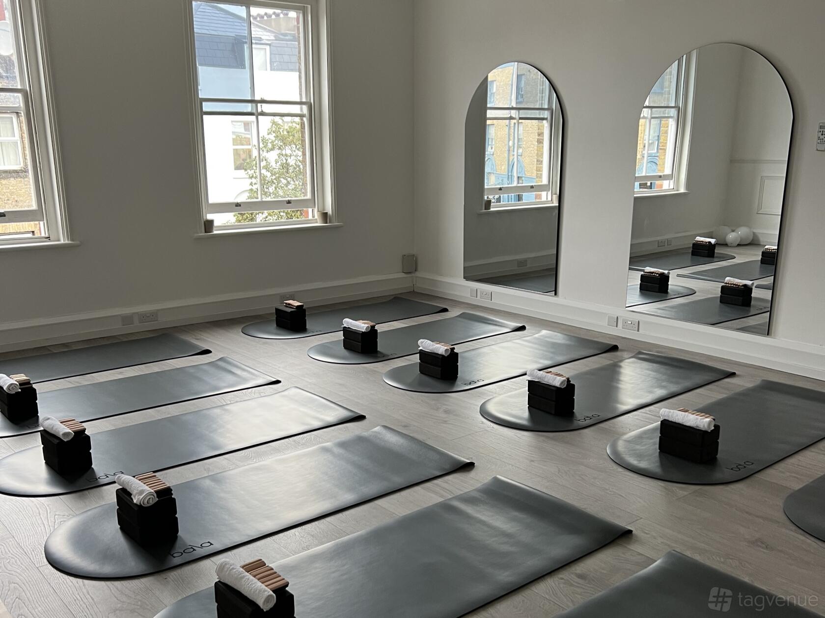 A yoga studio with black mats, yoga blocks, and large mirrors beside tall windows at Breathe Studio.