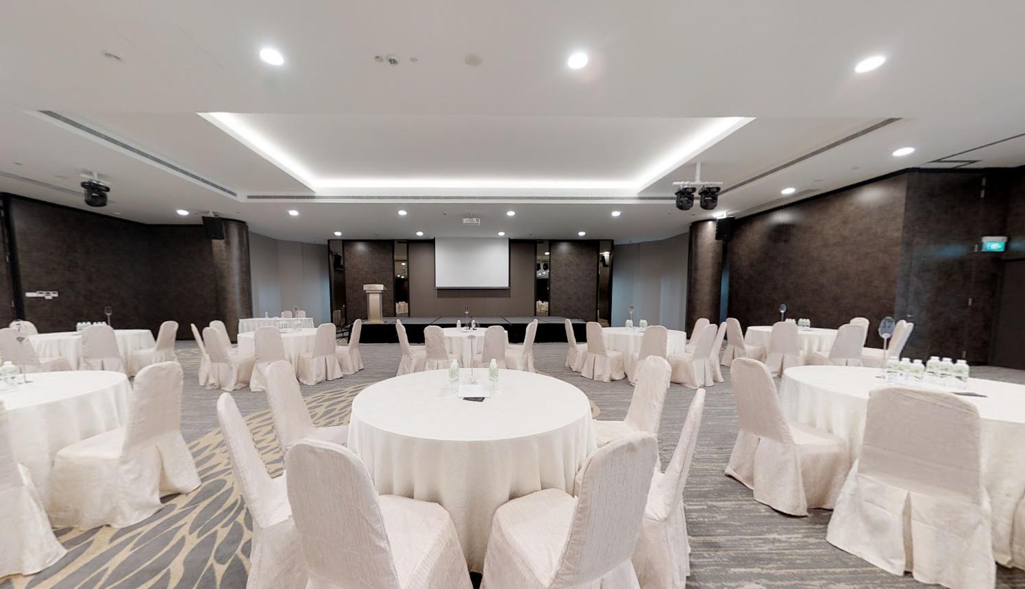 A banqueting hall with round tables draped in white linens arranged across a spacious ballroom at The Chevrons.