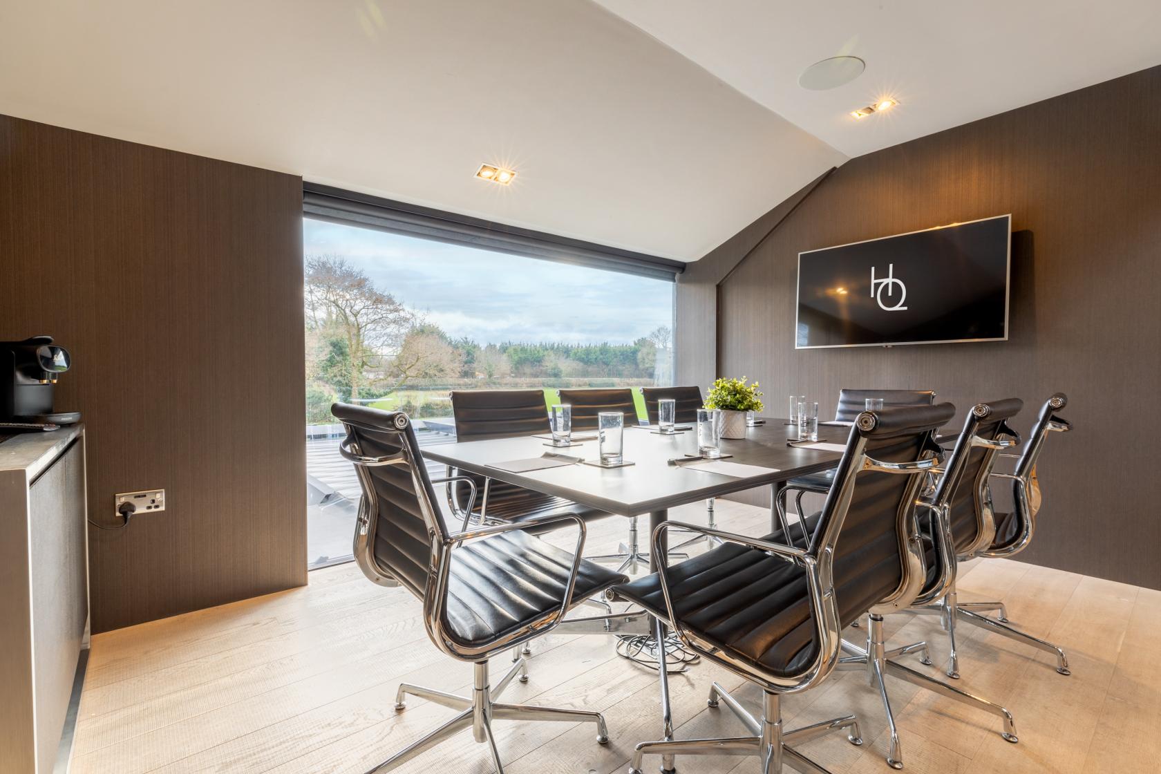 A meeting room with floor-to-ceiling windows, black leather chairs around a rectangular table, and a wall-mounted screen at The Colony HQ.