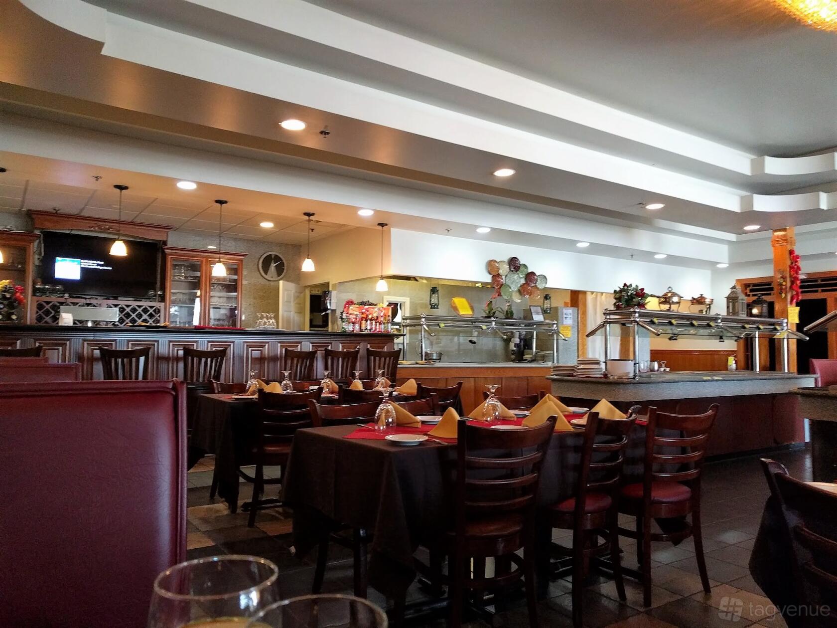 A dining room with dark wood chairs, tables set with folded napkins, and open kitchen area at Moon Indian Cuisine.