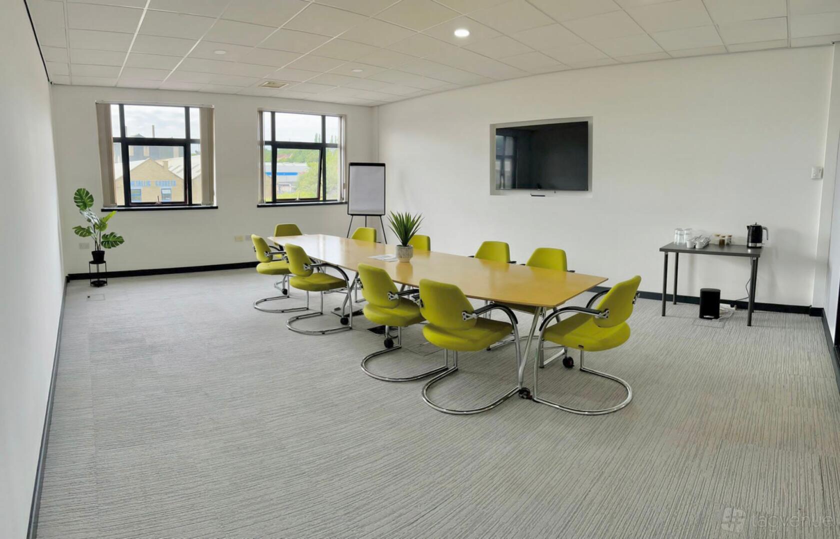 A meeting room with a long wooden table, green chairs, wall-mounted screen, and large windows at Lawrence House - Hub26.