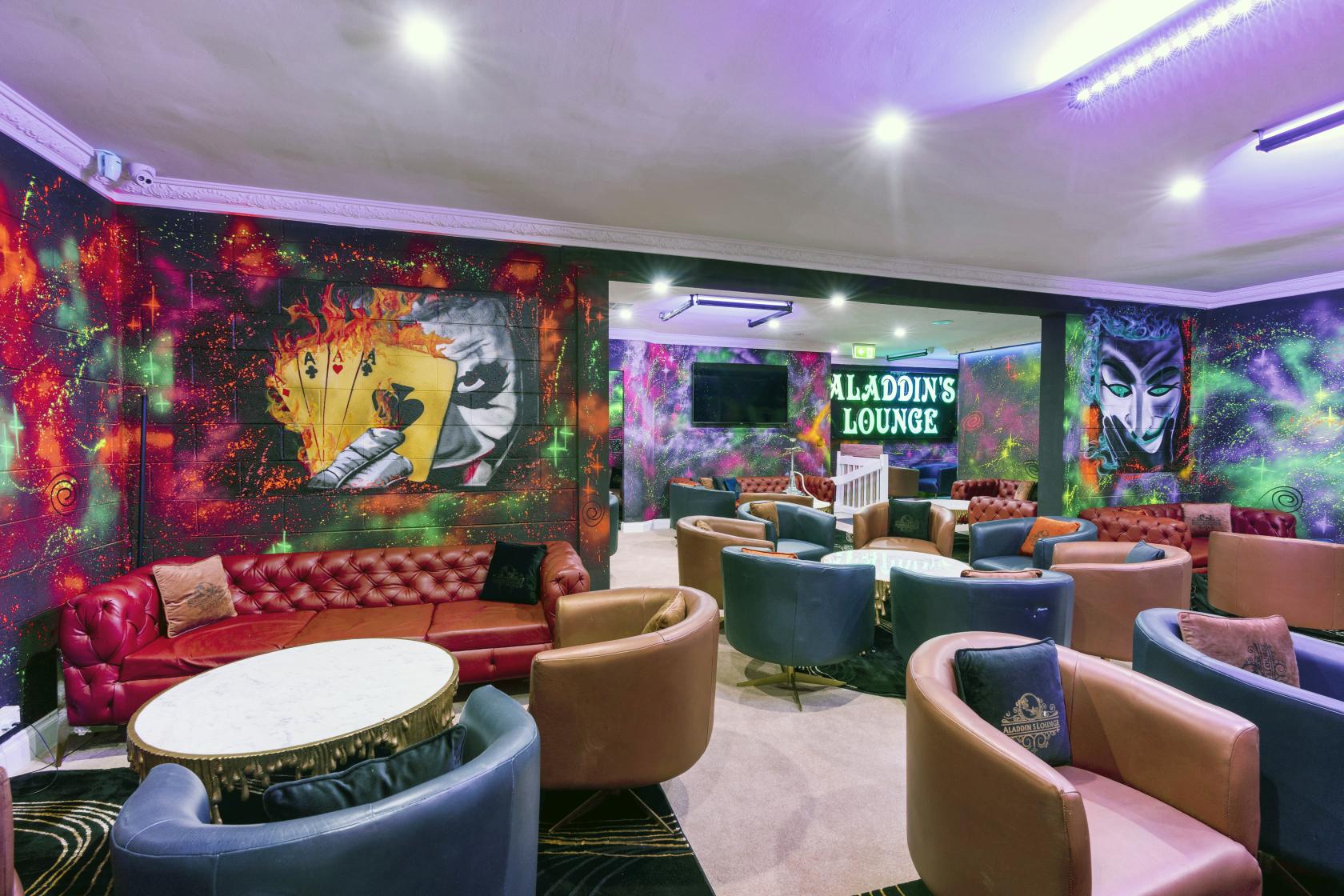 A lounge with colorful mural walls, round marble tables, and leather armchairs at Aladdin's Lounge.