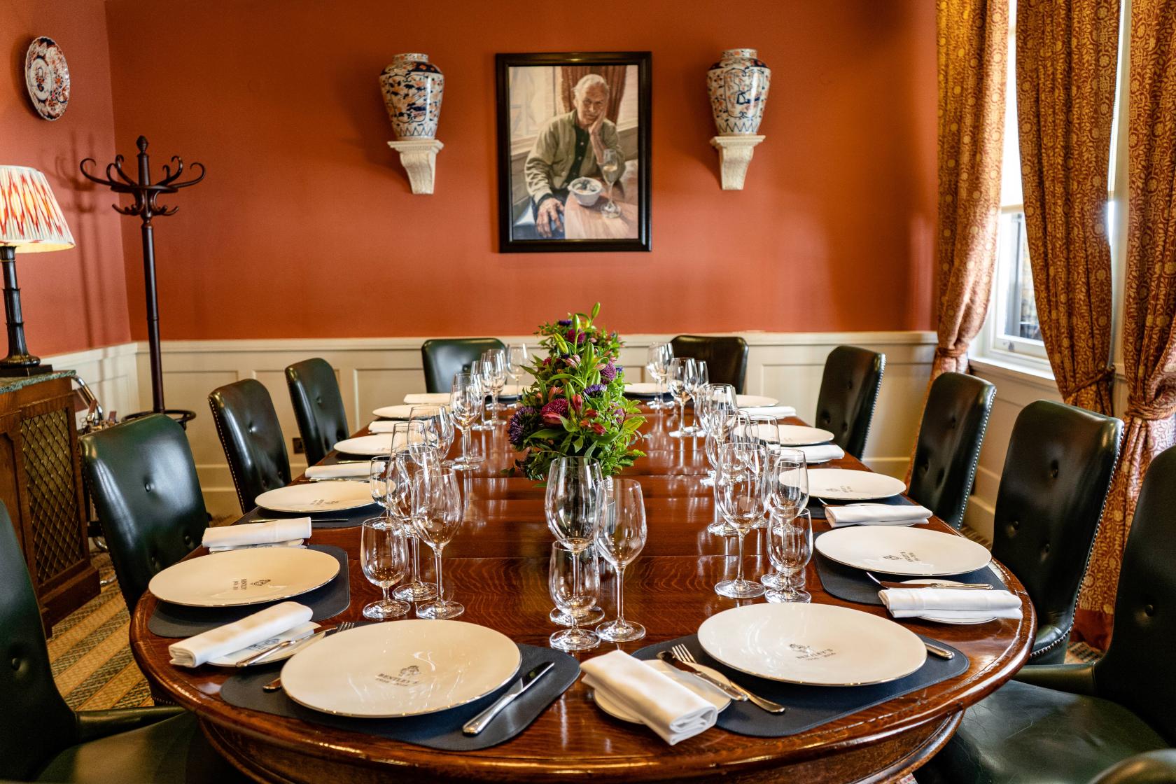 A dining room with a long oval table set with white plates, glassware, and green leather chairs at Bentley's Oyster Bar & Grill.