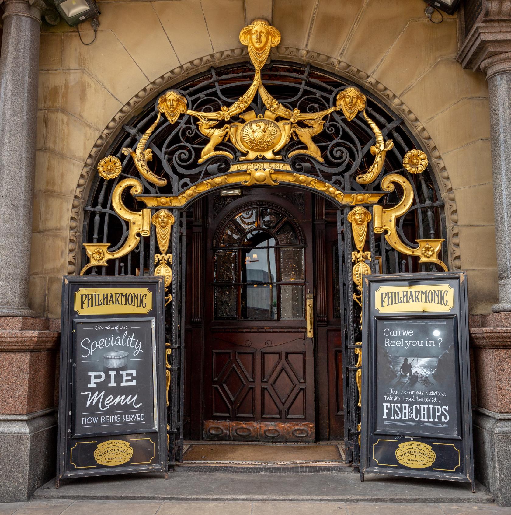 A pub with ornate gold decorative entrance and chalkboard menus at The Philharmonic Dining Rooms.