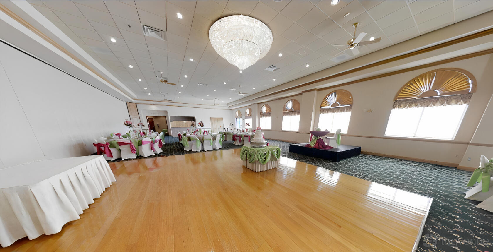 An event venue with a polished wood dance floor, chandelier lighting, and banquet tables with green sashes at Jennifer's Garden.