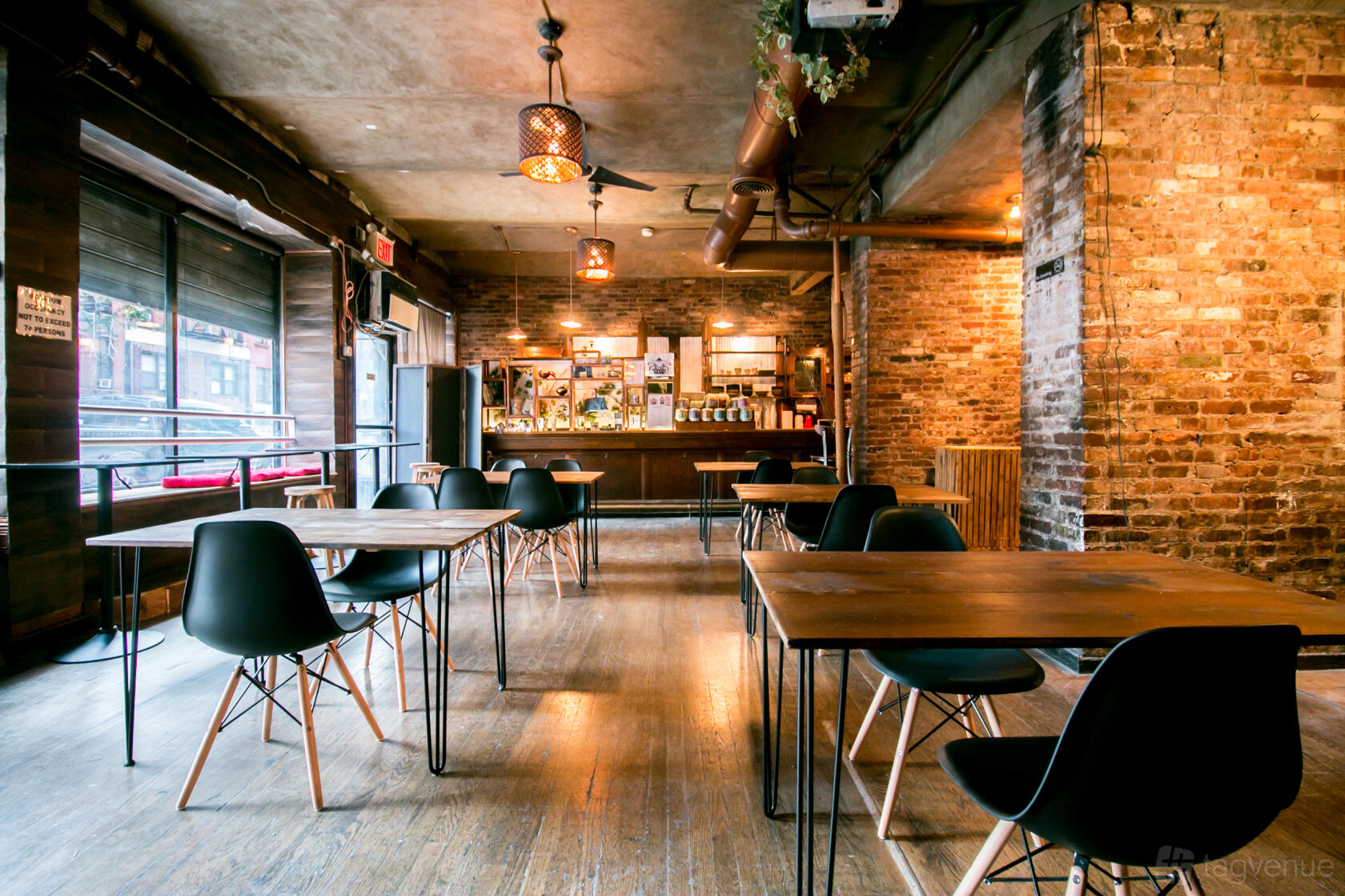 An event venue with exposed brick walls, wooden floors, and wooden tables with black chairs at Exposed Brick Multi-Use Event Space.