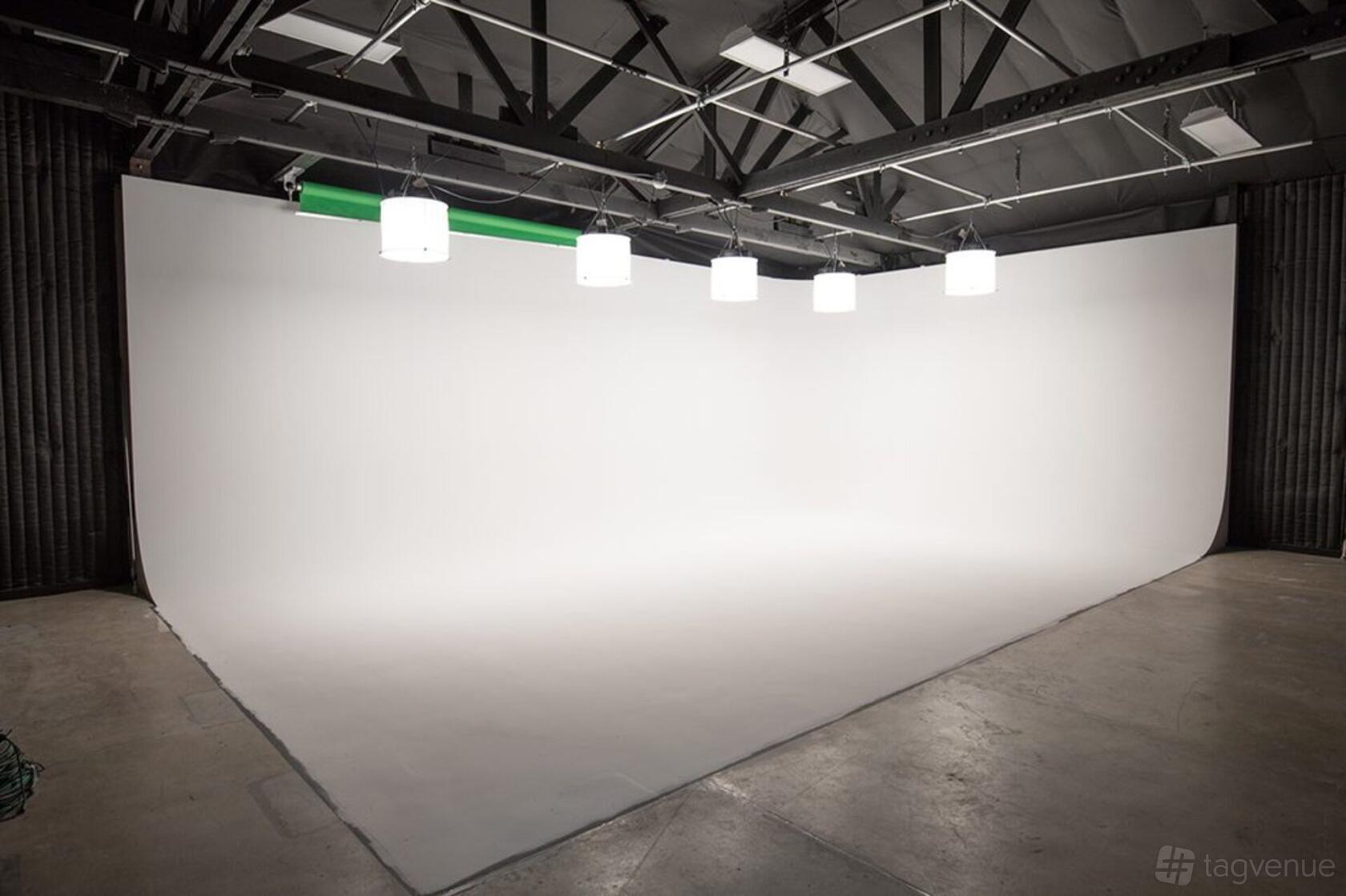 A photo studio with a seamless white cyclorama wall, overhead studio lights, and exposed ceiling at Stray Angel Films.