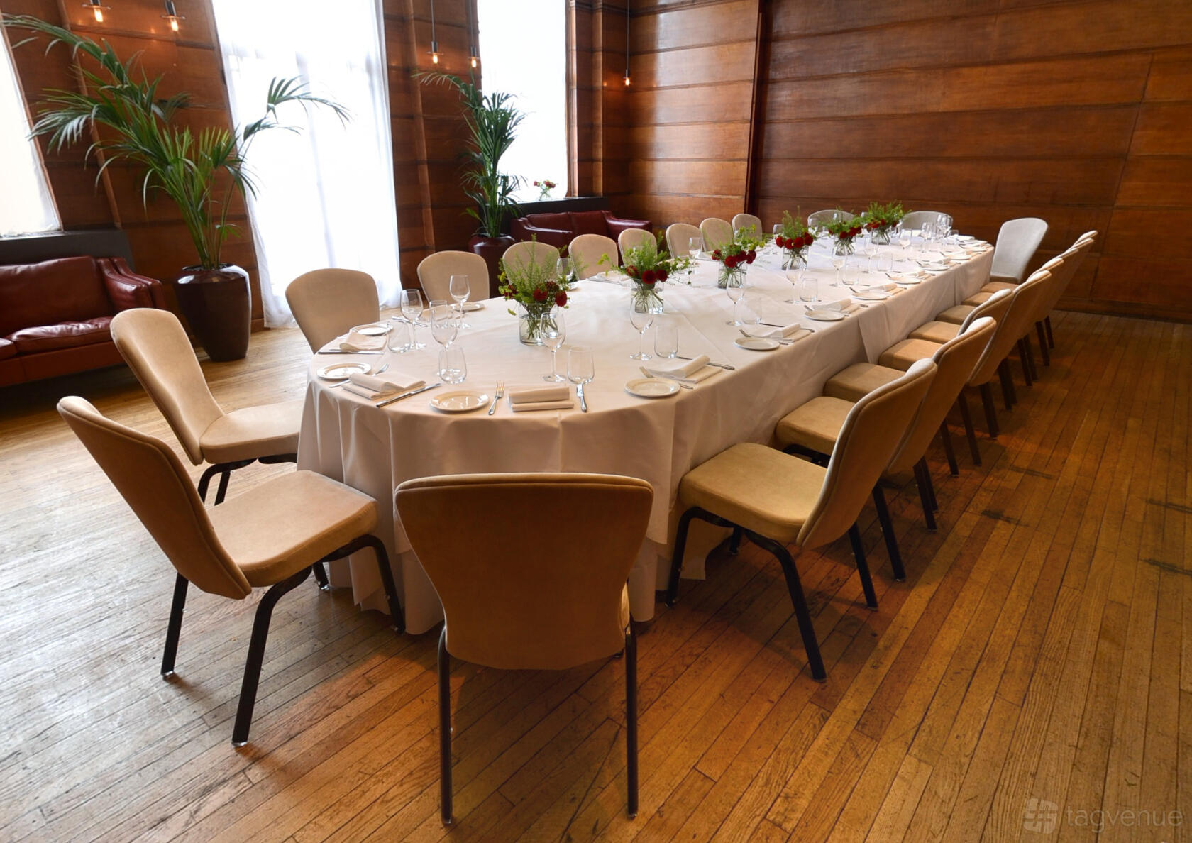 A hotel hall with wood-paneled walls, floor-to-ceiling windows, and a U-shaped table set for dining at Town Hall Hotel.