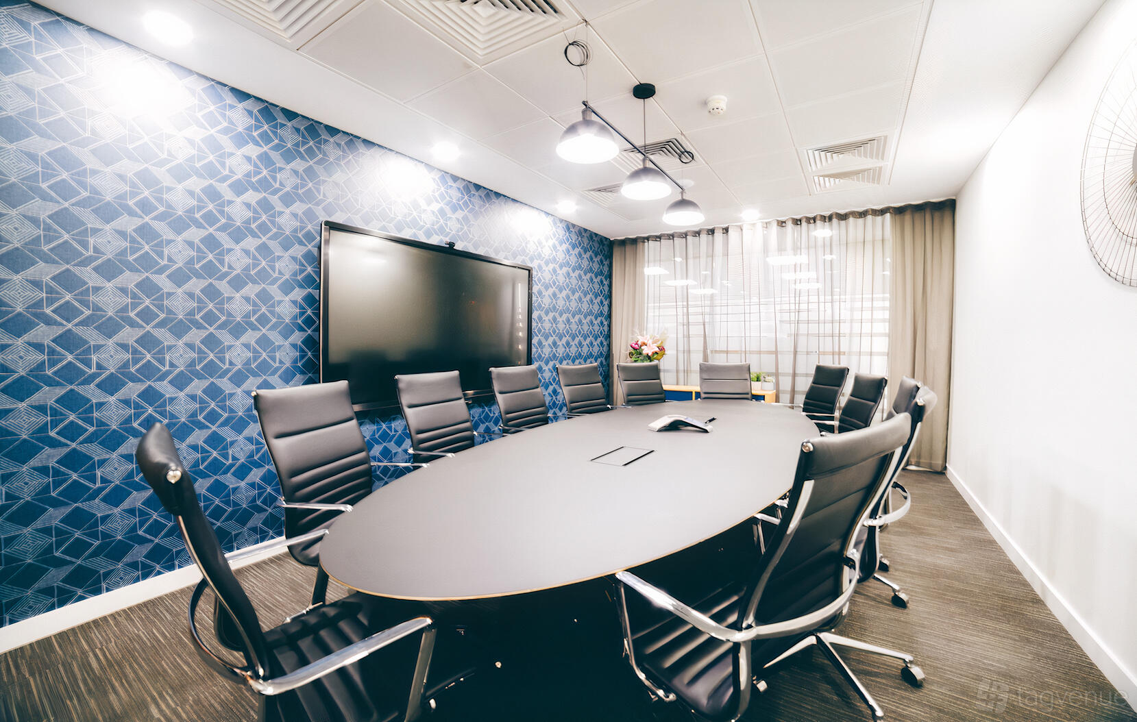 A meeting centre with an oval conference table, black chairs, and a large display screen at Orega Leeds.