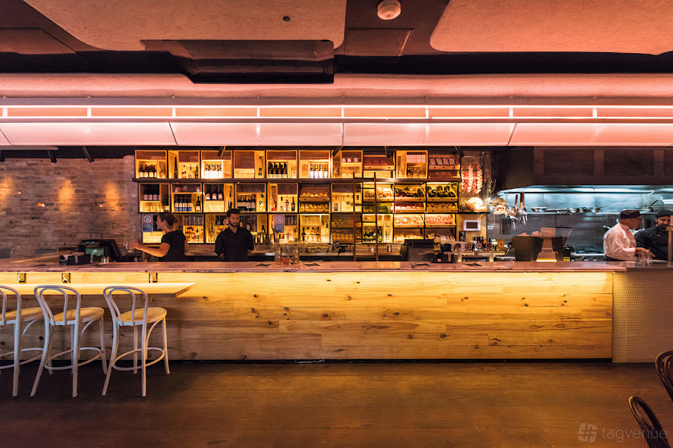 A hotel bar with a long wooden counter, illuminated backlit shelving, and exposed brick walls at Phoenix Hotel.