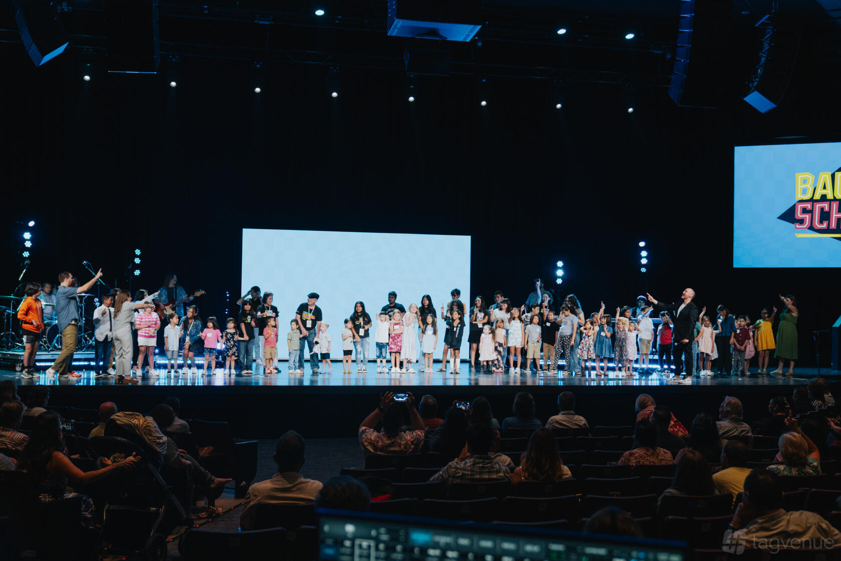 An auditorium with tiered seating, a large stage, LED spotlights, and dual projection screens at LifeAustin Mueller.