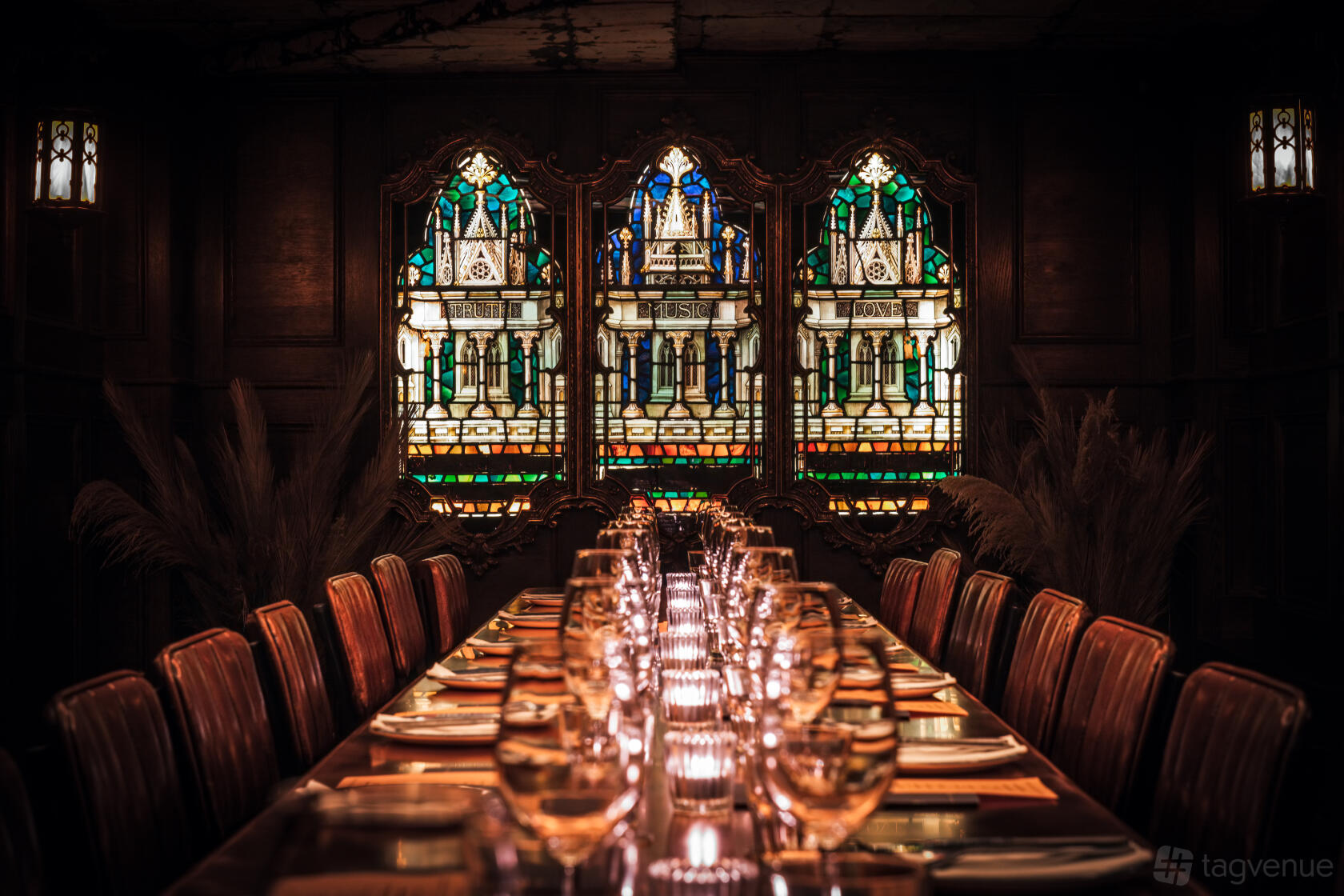 A dining room with a long wooden table, leather chairs, and stained glass windows at The Blues Kitchen Manchester.