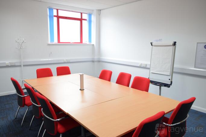 A training room with a large rectangular table, red chairs, a flip chart, and a window at Humanitarian Academy for Development.