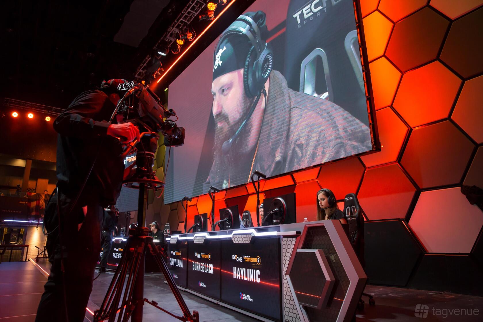An esports event venue with illuminated gaming stations, a large video screen, and hexagonal wall panels at HyperX Arena Las Vegas.