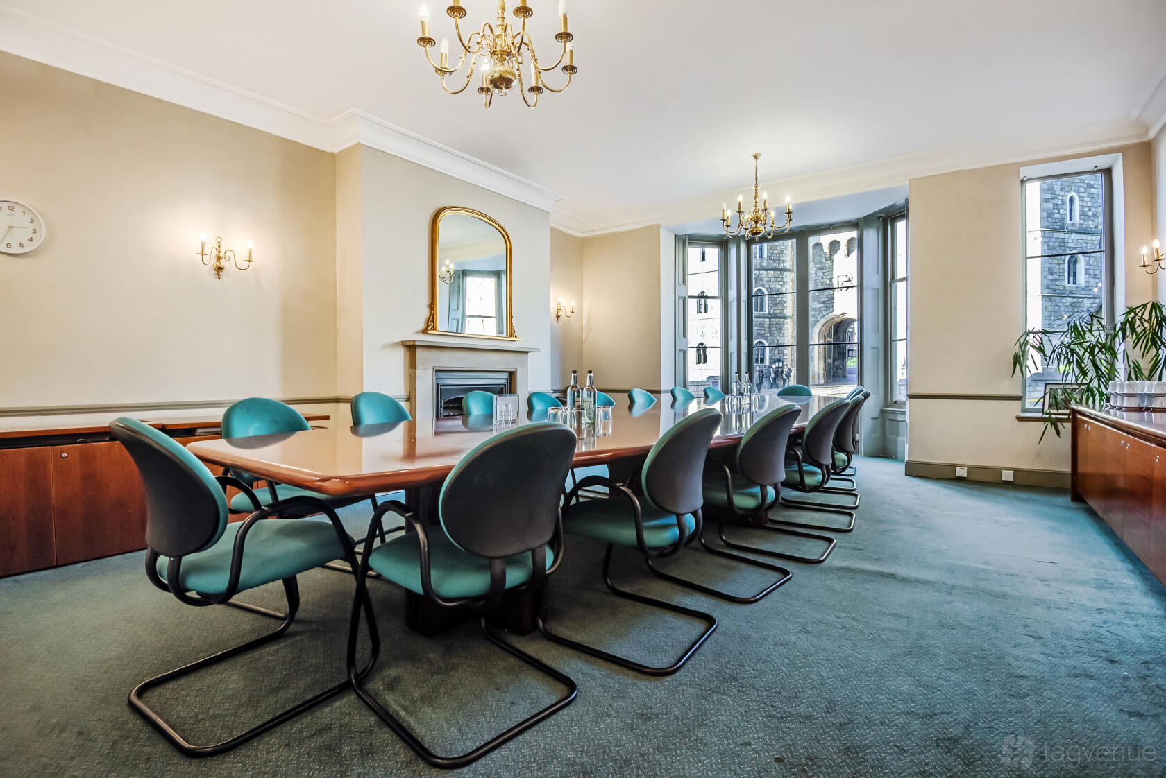 A meeting room with a long wood conference table, modern chairs, tall windows, chandeliers, and a fireplace at Castle Hill House.