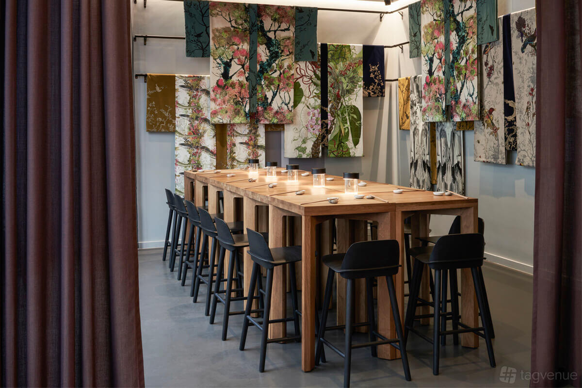 A private dining room with a long wooden table, black chairs, and colorful kimono fabrics on the walls at Sticks'n'Sushi Canary Wharf.