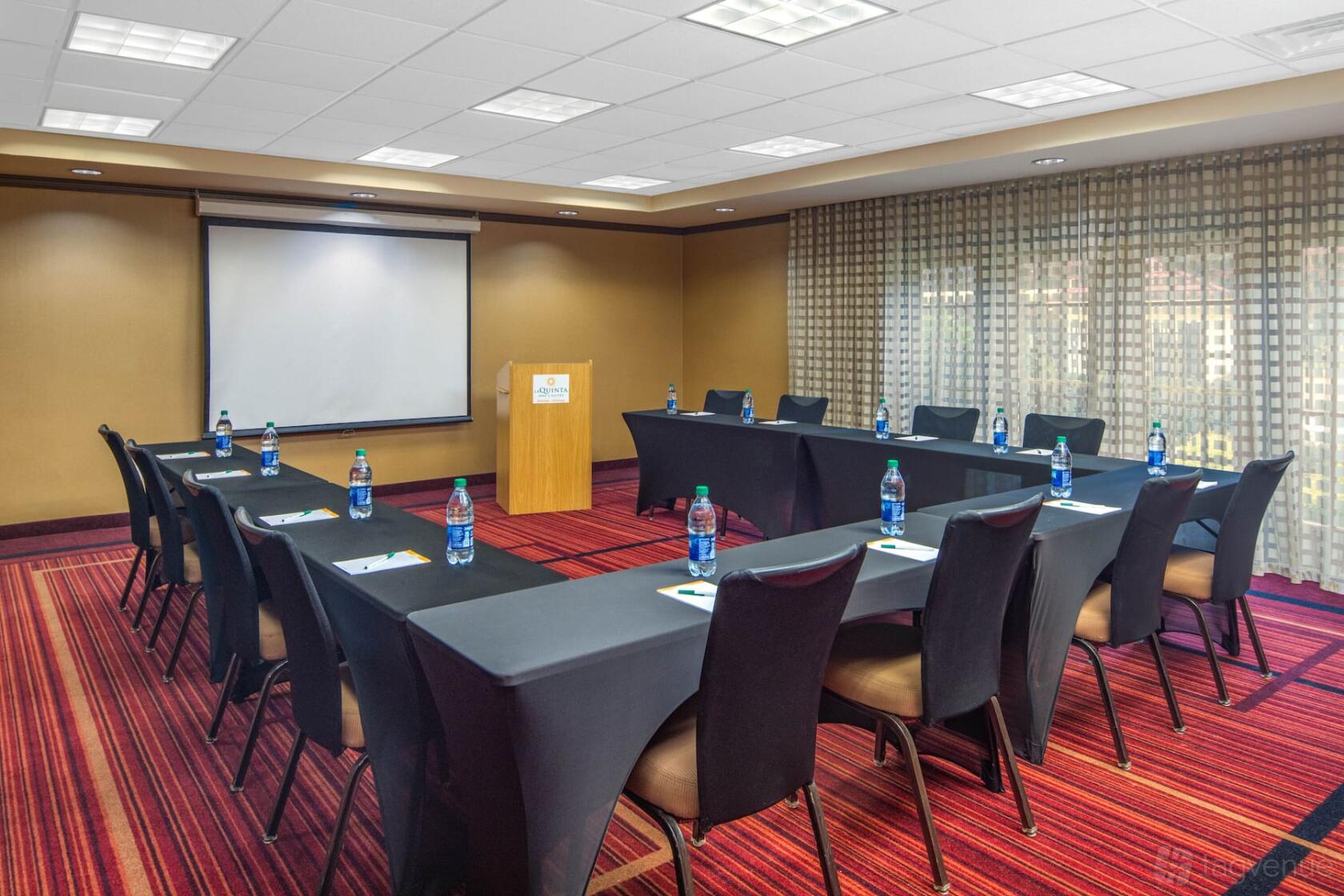 A meeting room with U-shaped black table setup, red patterned carpet, and floor-to-ceiling windows at La Quinta Inn & Suites Atlanta Ballpark.