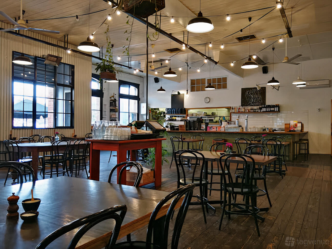 An event space in a cafe with wooden floors, black bentwood chairs, string lights, and large windows at Brunswick Foodstore.