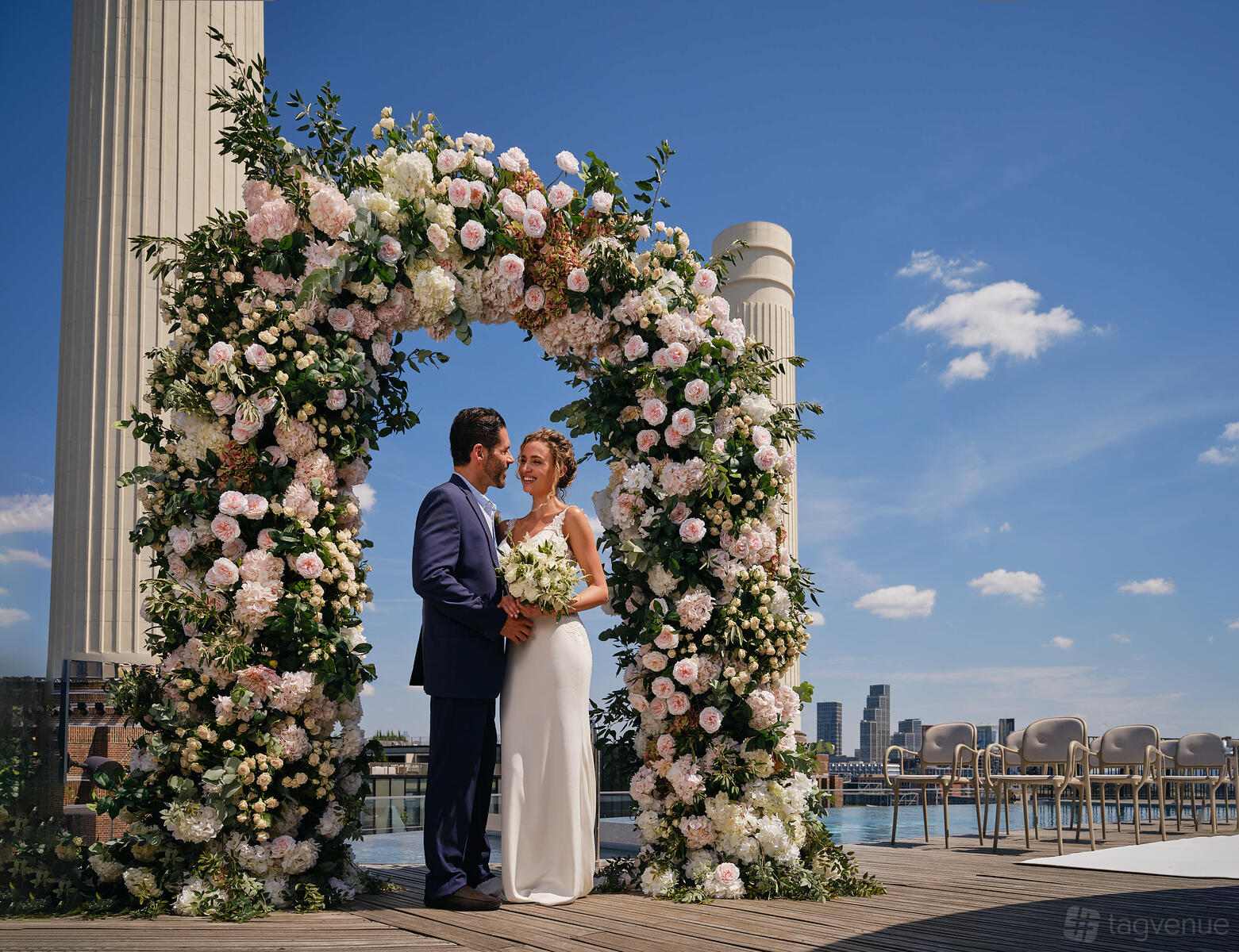 A rooftop venue with a floral wedding arch, city skyline views, and rows of chairs at art'otel London Battersea Power Station.
