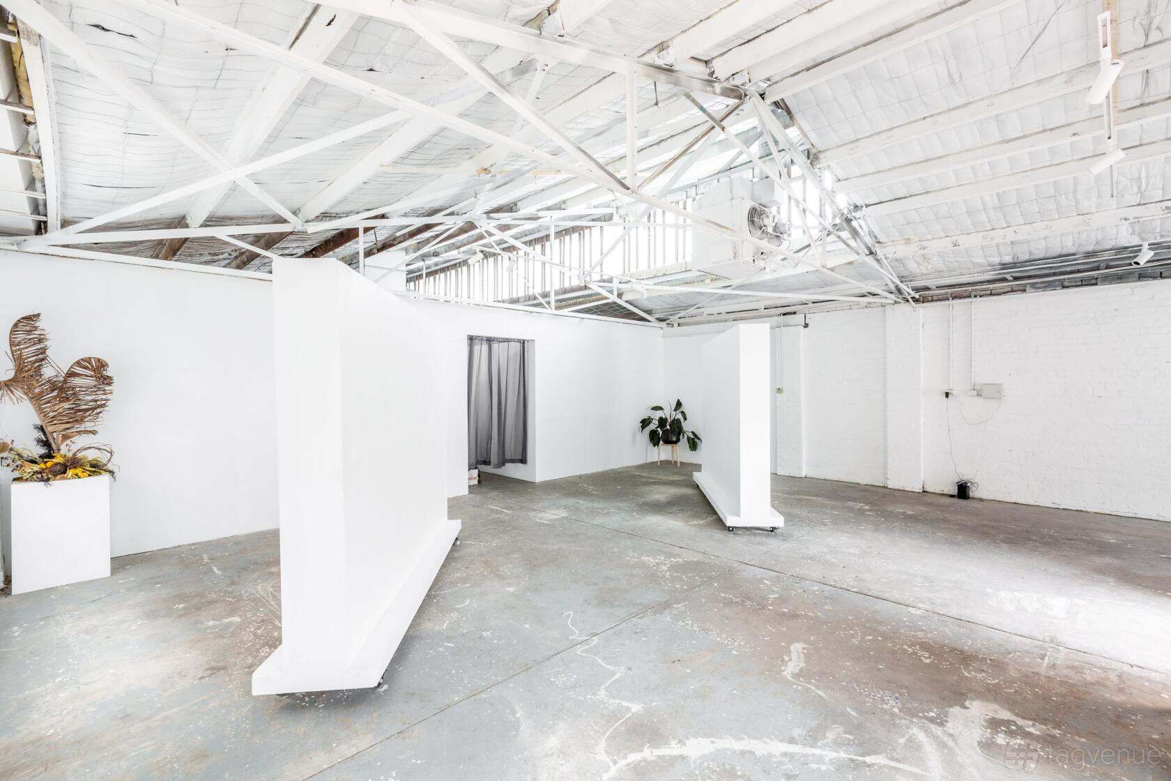 An event space in a warehouse with white painted walls, exposed beams, and concrete floors at Honey Bones Gallery.