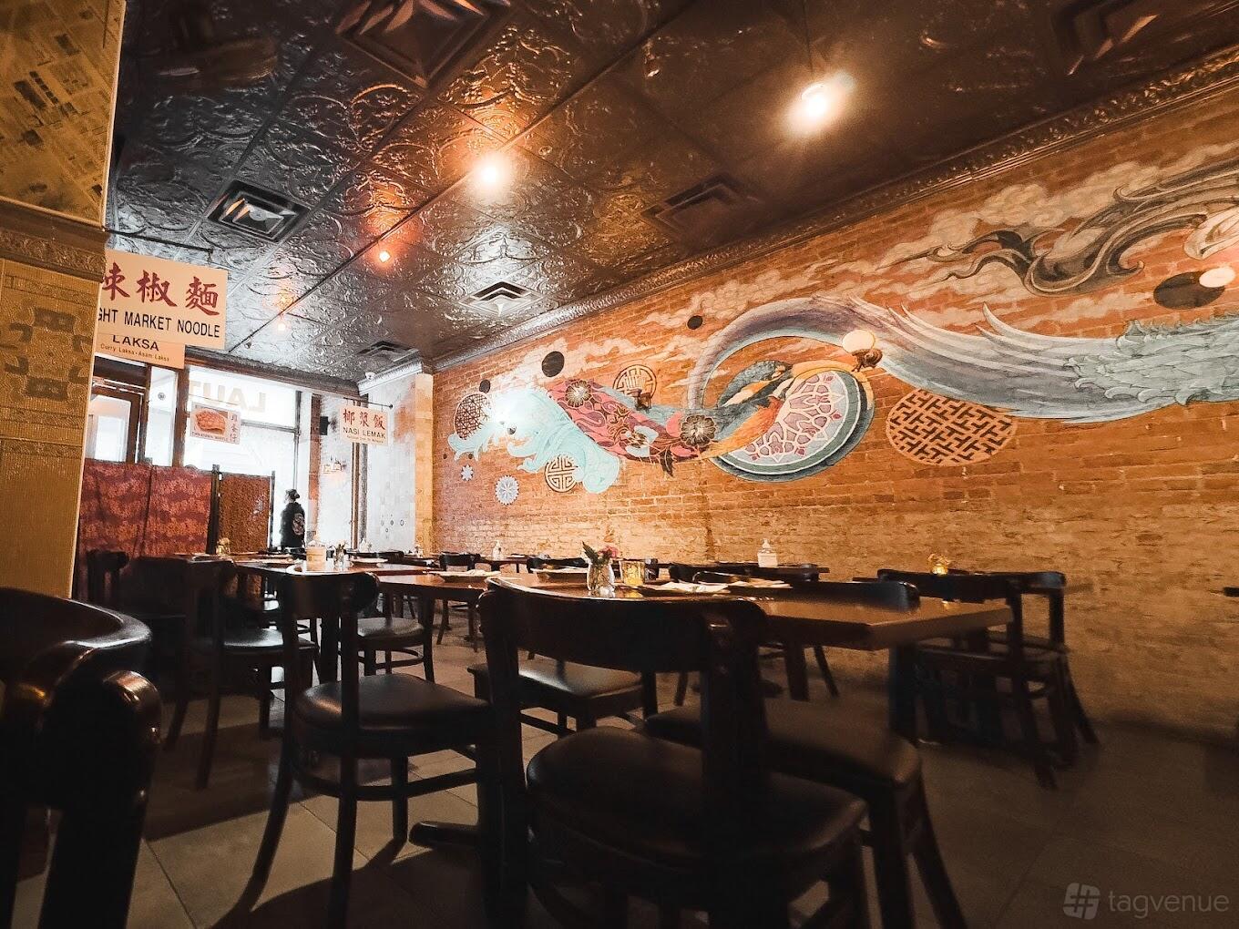 A restaurant with exposed brick walls, colorful mural, dark wood tables, and warm lighting at Laut.