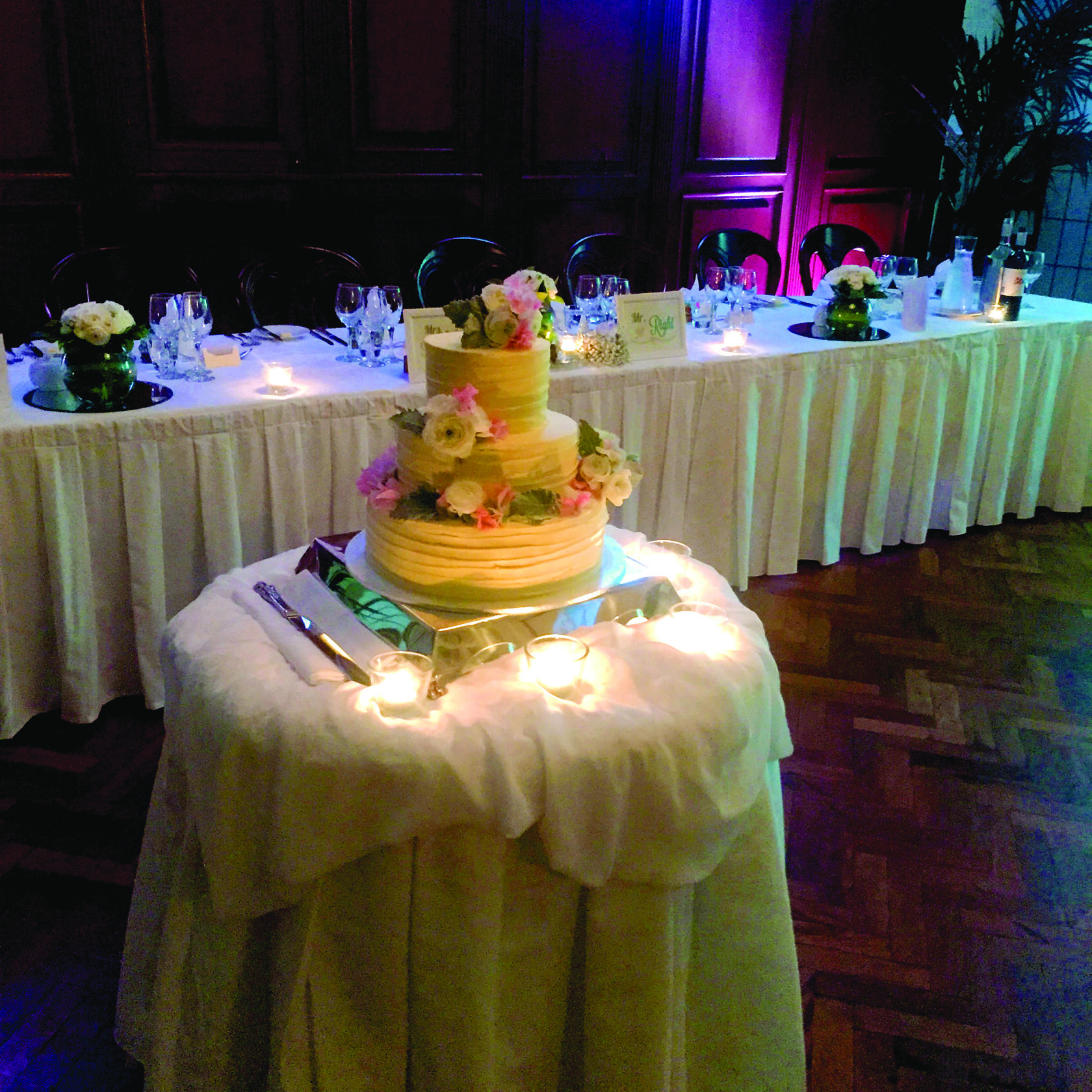 A hotel hall with a round table featuring a tiered wedding cake, candles, and floral arrangements at The Castlereagh Boutique Hotel.