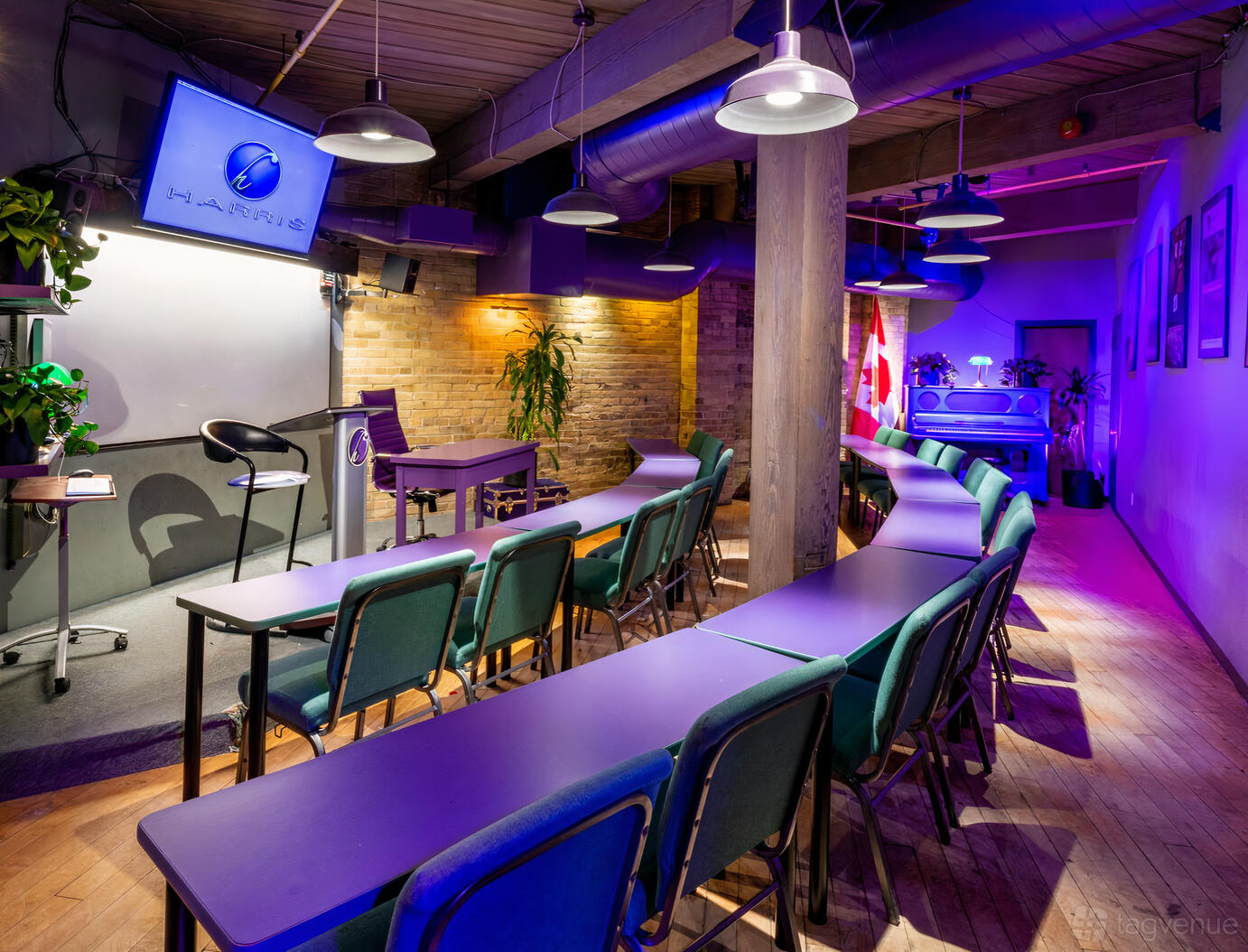 A meeting centre classroom with curved tables, green chairs, exposed brick walls, and ceiling ducts at Harris Institute.