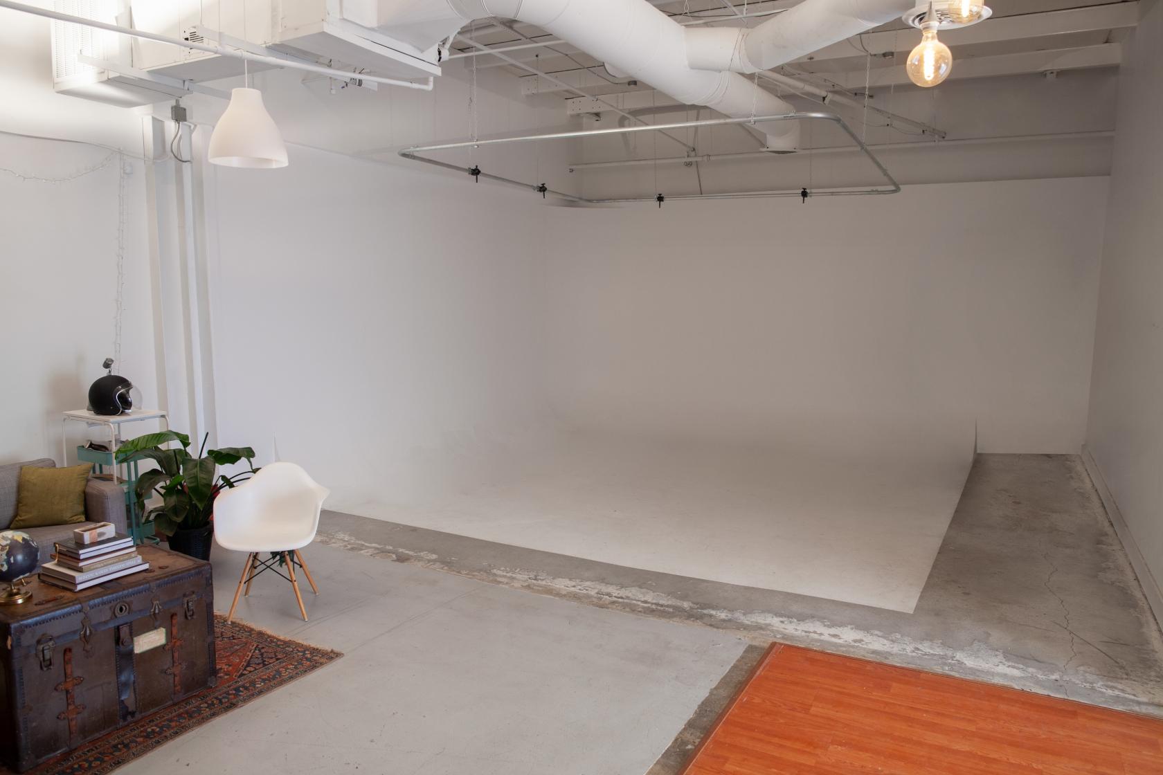 A photo studio with a large white cyclorama wall, exposed ductwork, and a lounge area at Raider Films / Rise Studios.