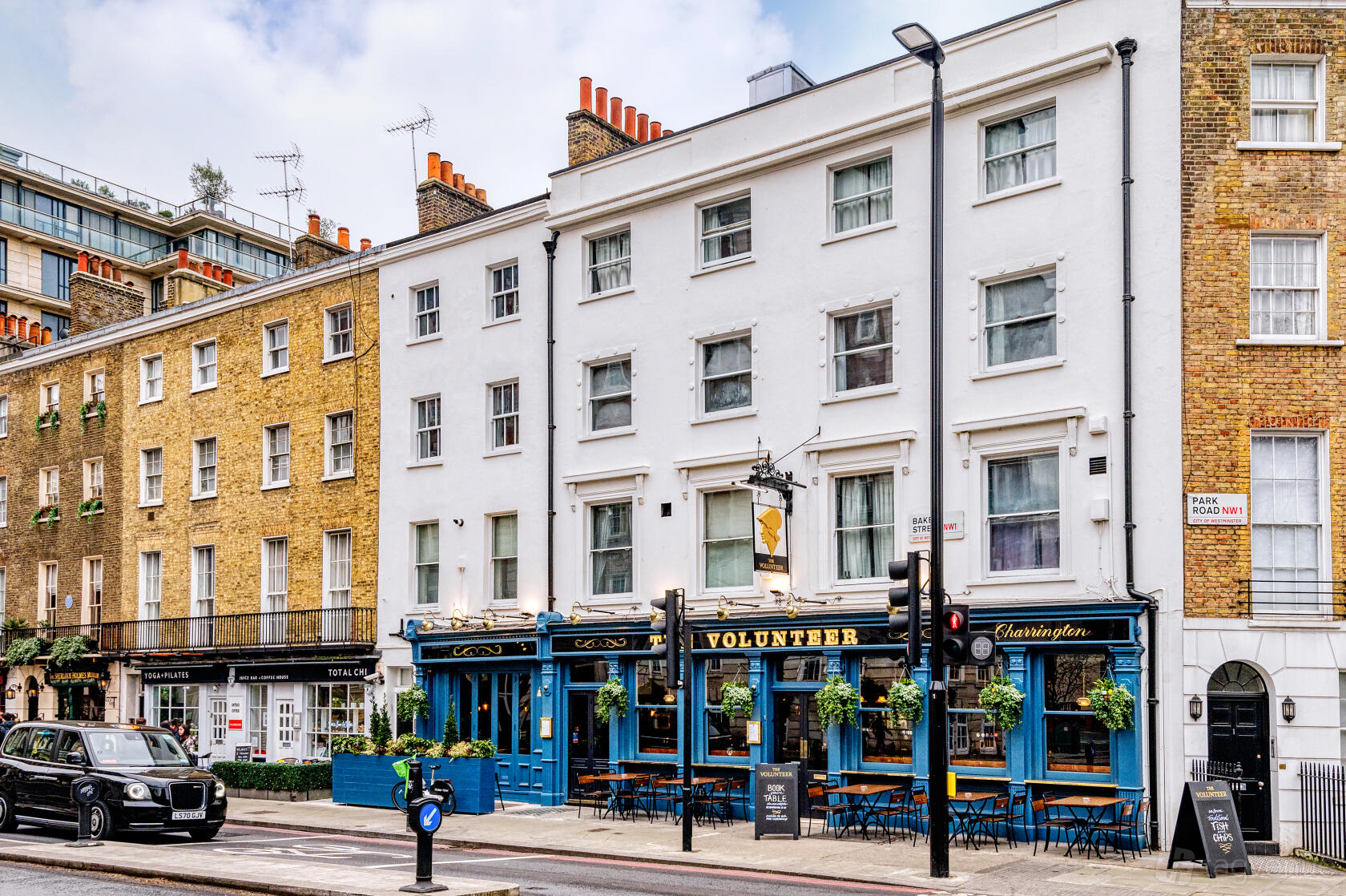 A pub with a blue exterior, hanging flower baskets, and outdoor seating at The Volunteer, Baker Street.