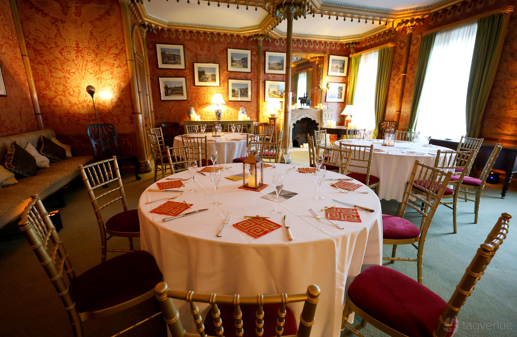 An event space in a museum with round tables, gold chairs, ornate red walls, and framed artwork at Royal Pavilion.