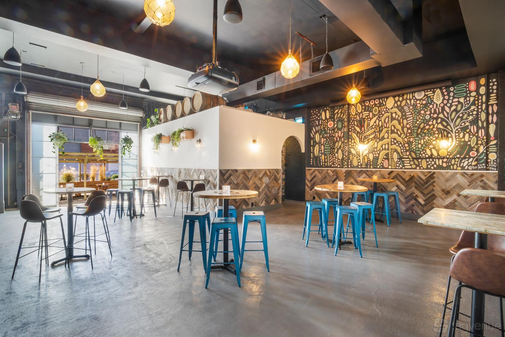 An event space with high ceilings, hanging lights, barrel decor, and wooden tables with metal stools at Keg & Lantern Brewery.