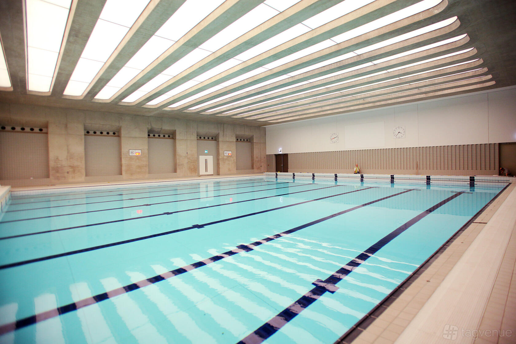An indoor swimming pool with lane dividers, high ceilings, and bright overhead lighting at London Aquatics Centre.