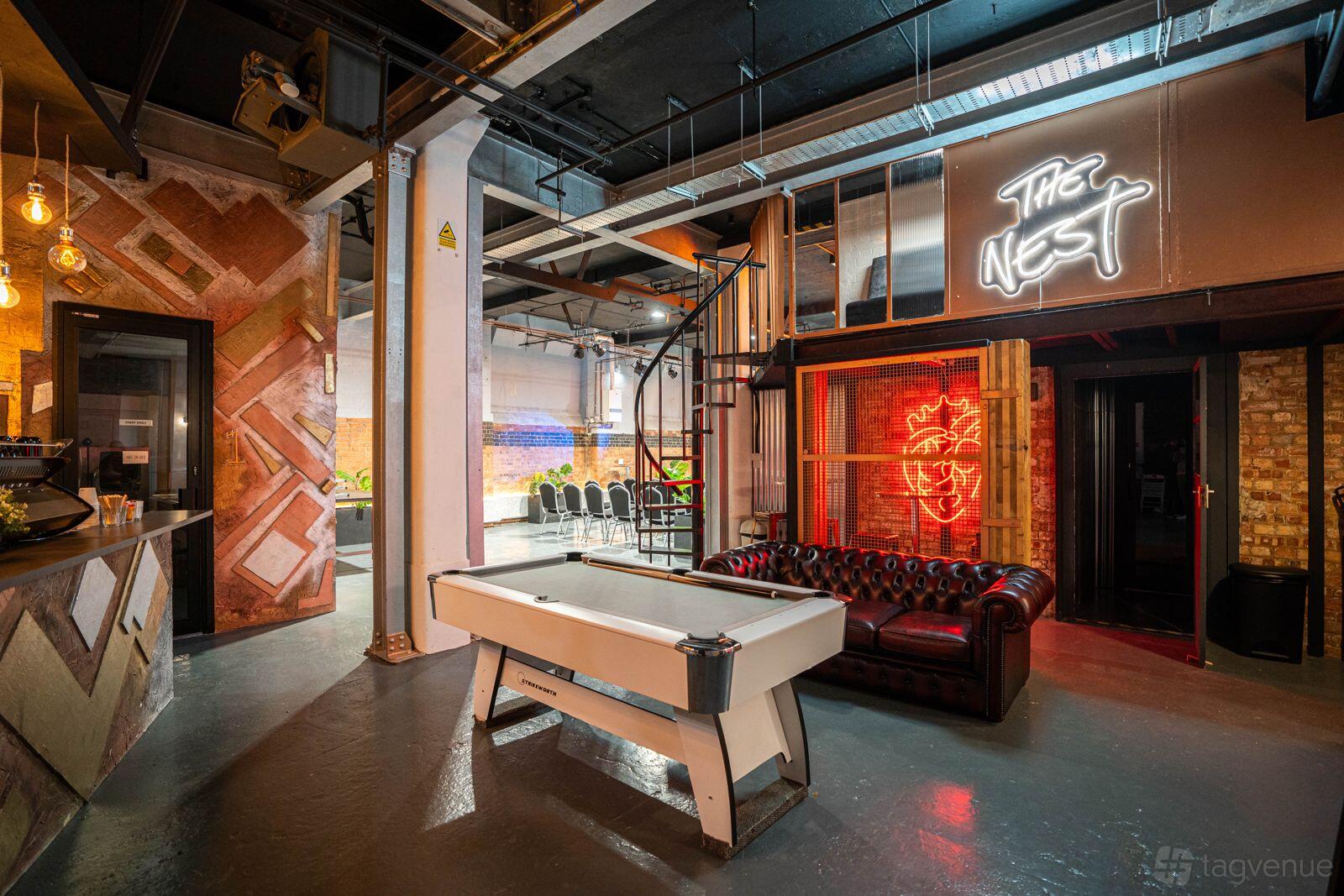A community hall with a white air hockey table, exposed brick walls, leather sofa, and neon signs at The Cave.