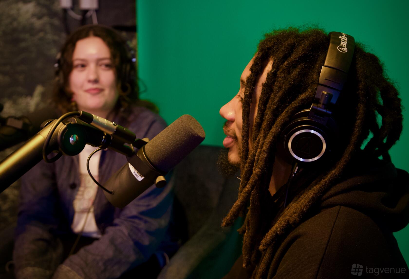 A coworking space with a green backdrop, microphones, and headsets in the podcast production room at Techspace Shoreditch.