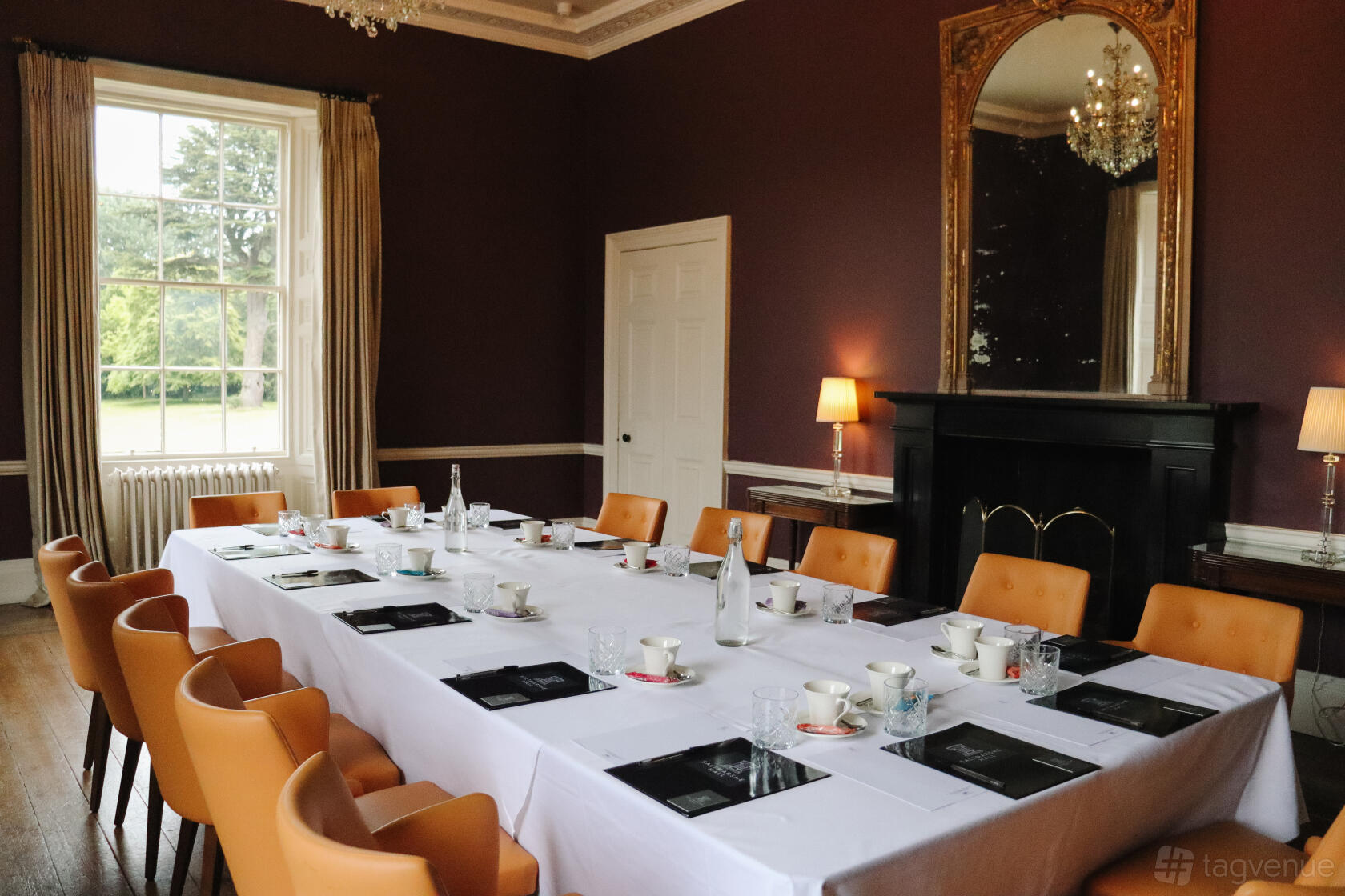 A conference room with a long table, tan chairs, chandeliers, and large windows at Saltmarshe Hall.
