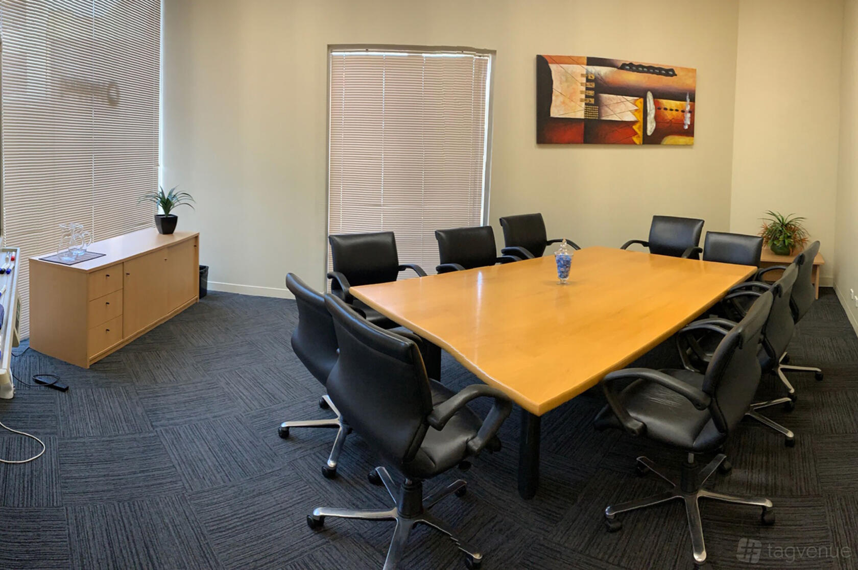 A boardroom with a large wooden conference table, black chairs, wall art, and natural light at Access Business Centres Balaclava.