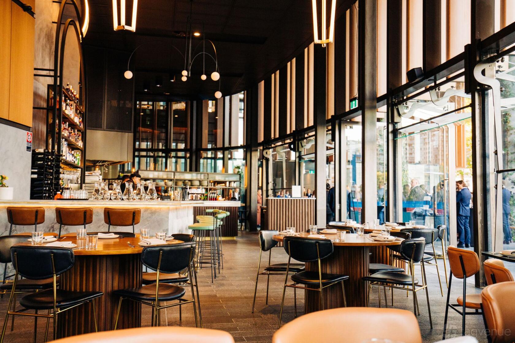 An event space in a restaurant with floor-to-ceiling windows, modern lighting, and round wooden tables at Willo Parramatta.