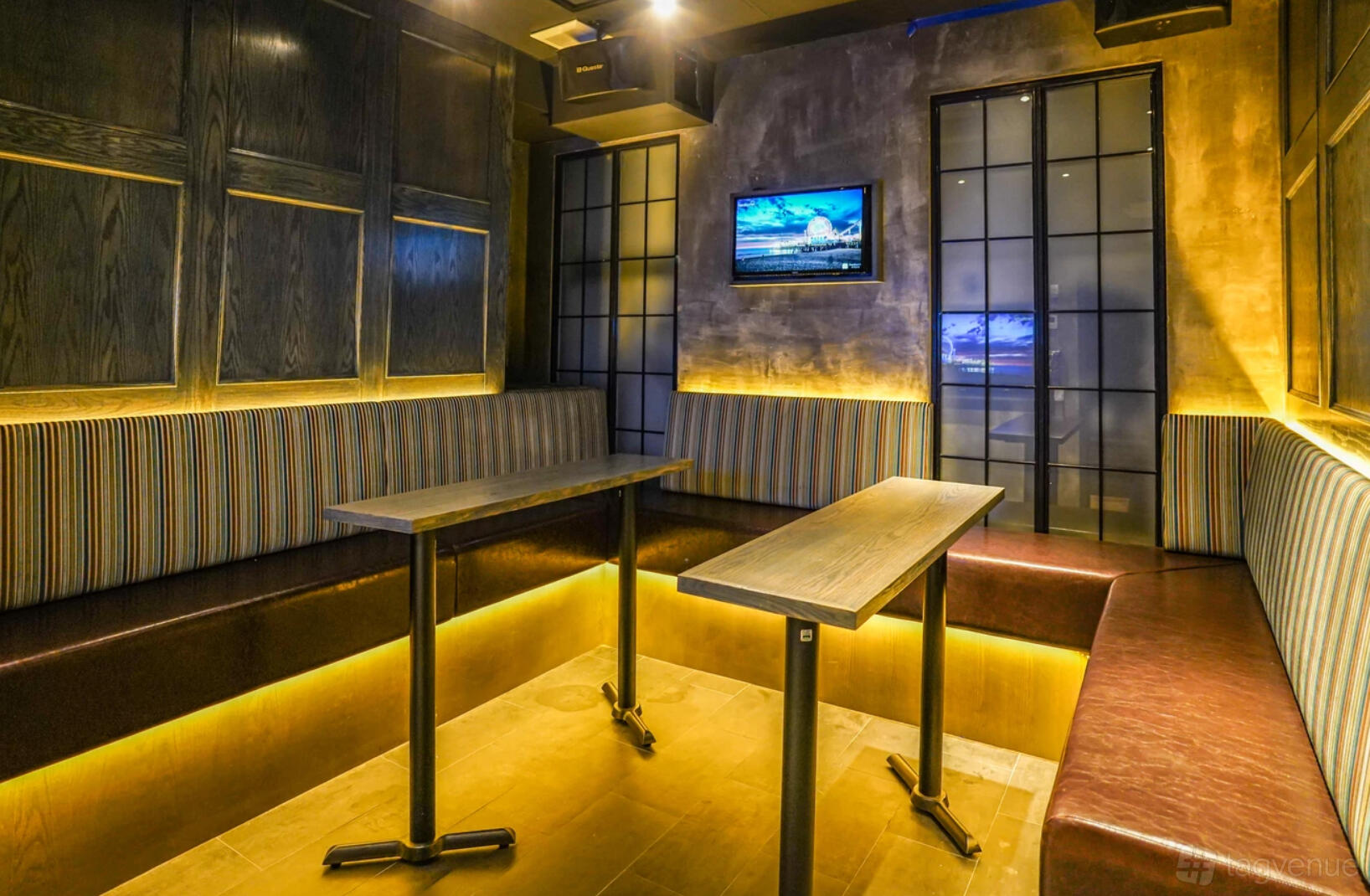 A private karaoke room with striped upholstered benches, wood tables, and a wall-mounted TV at MS. KIM'S Lounge & Private Karaoke.