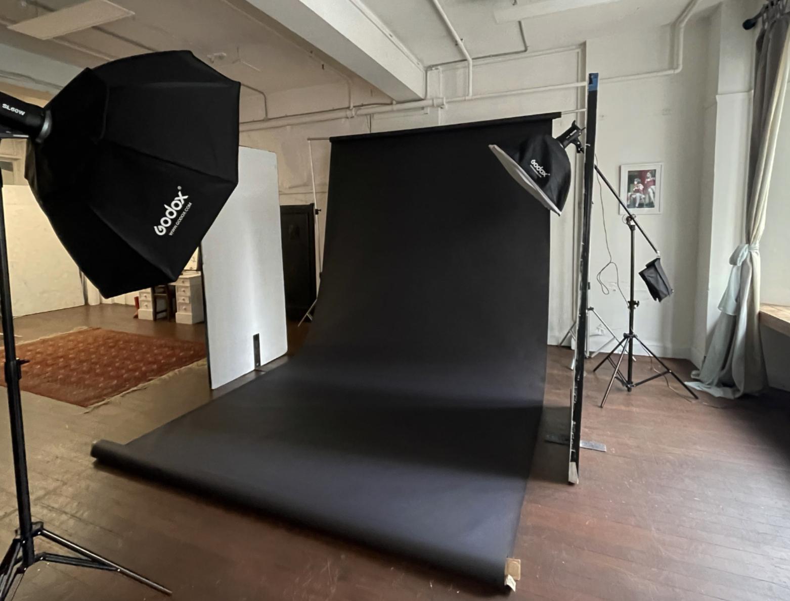 A photo studio with a seamless black backdrop, softbox lighting, and hardwood floors at Lolly Loft Studio.