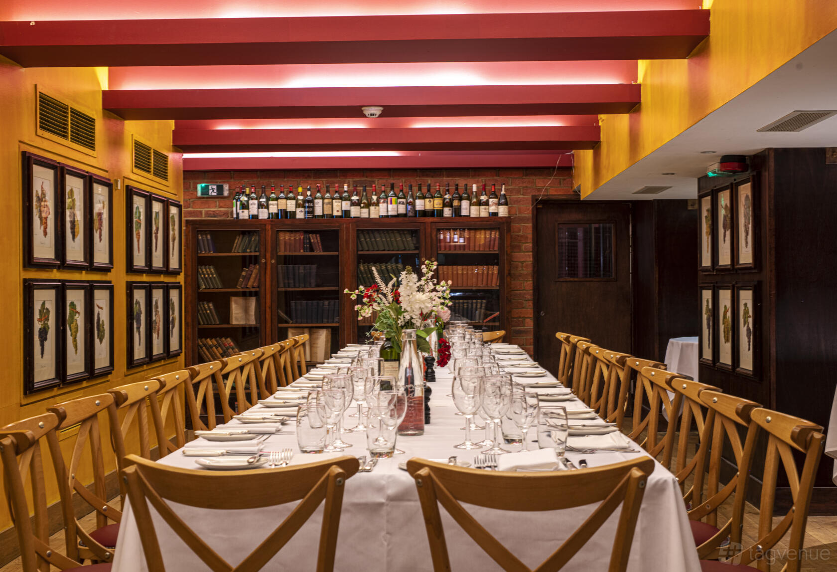 A dining room with a long table set with glassware and white linens, wooden chairs, floral centerpiece, and wall art at Bleeding Heart.