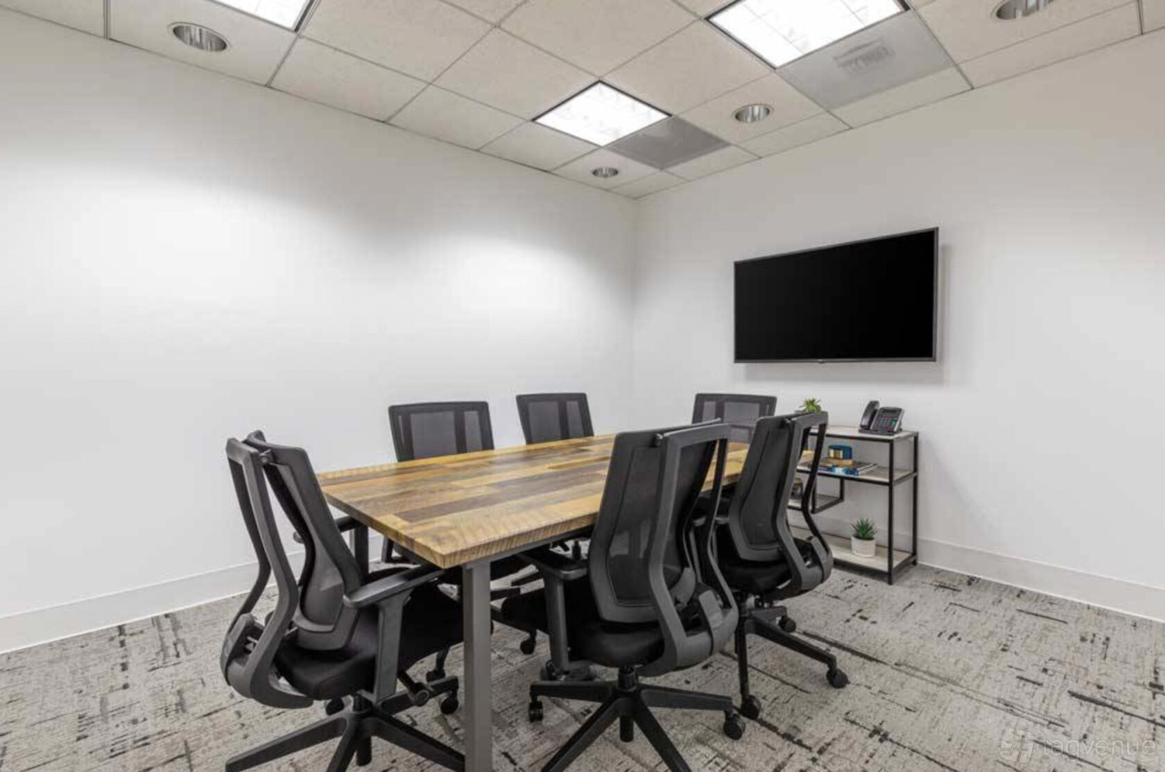 A coworking space with a wooden conference table, black office chairs, and wall-mounted TV at Premier Workspaces - Executive Tower.